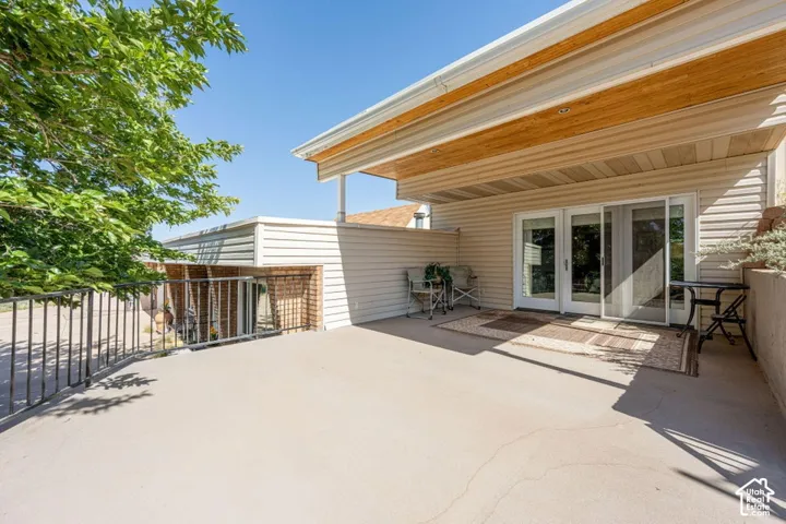 Spacious outdoor concrete patio featuring a partial overhead covering with wood-finish accents, a metal railing, and multiple glass door entries