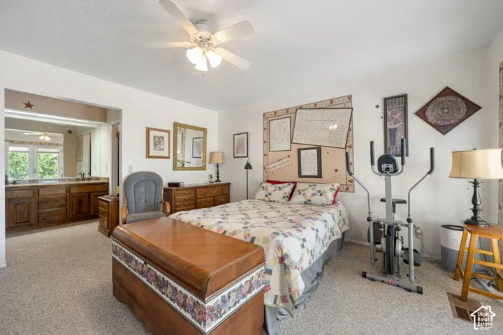 Carpeted room with an open entry to a bathroom featuring a dual vanity with wood-finish cabinetry and an overhead mirror