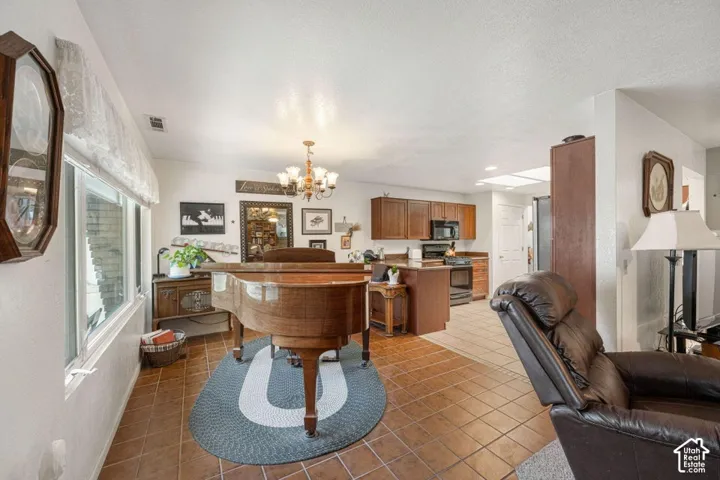 Open concept living area featuring terracotta-style tile flooring and a kitchen with wood-finish cabinetry, black appliances, and a central island