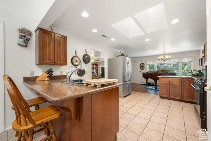 Kitchen featuring recessed lighting, a breakfast bar with seating, a stainless steel sink with a gooseneck faucet, tile flooring, and two skylights
