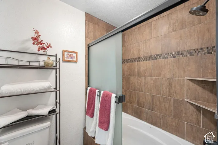 Bathtub with ceramic tile surround, decorative mosaic accent band, and integrated corner shelving