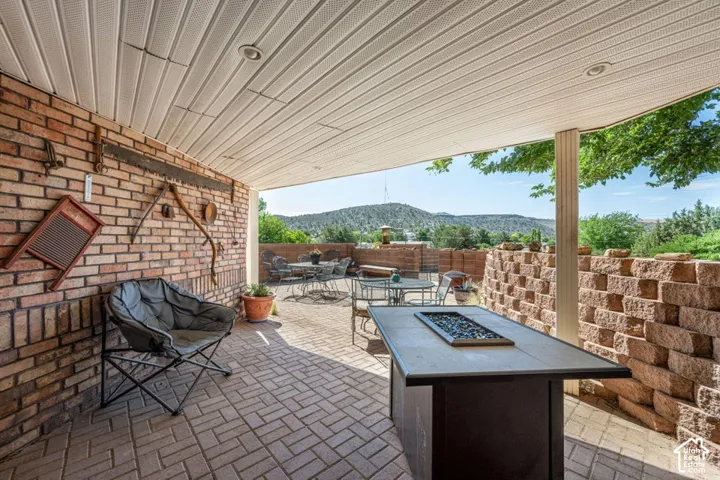 Covered patio featuring brick-laid flooring, recessed lighting, and a stone-clad retaining wall
