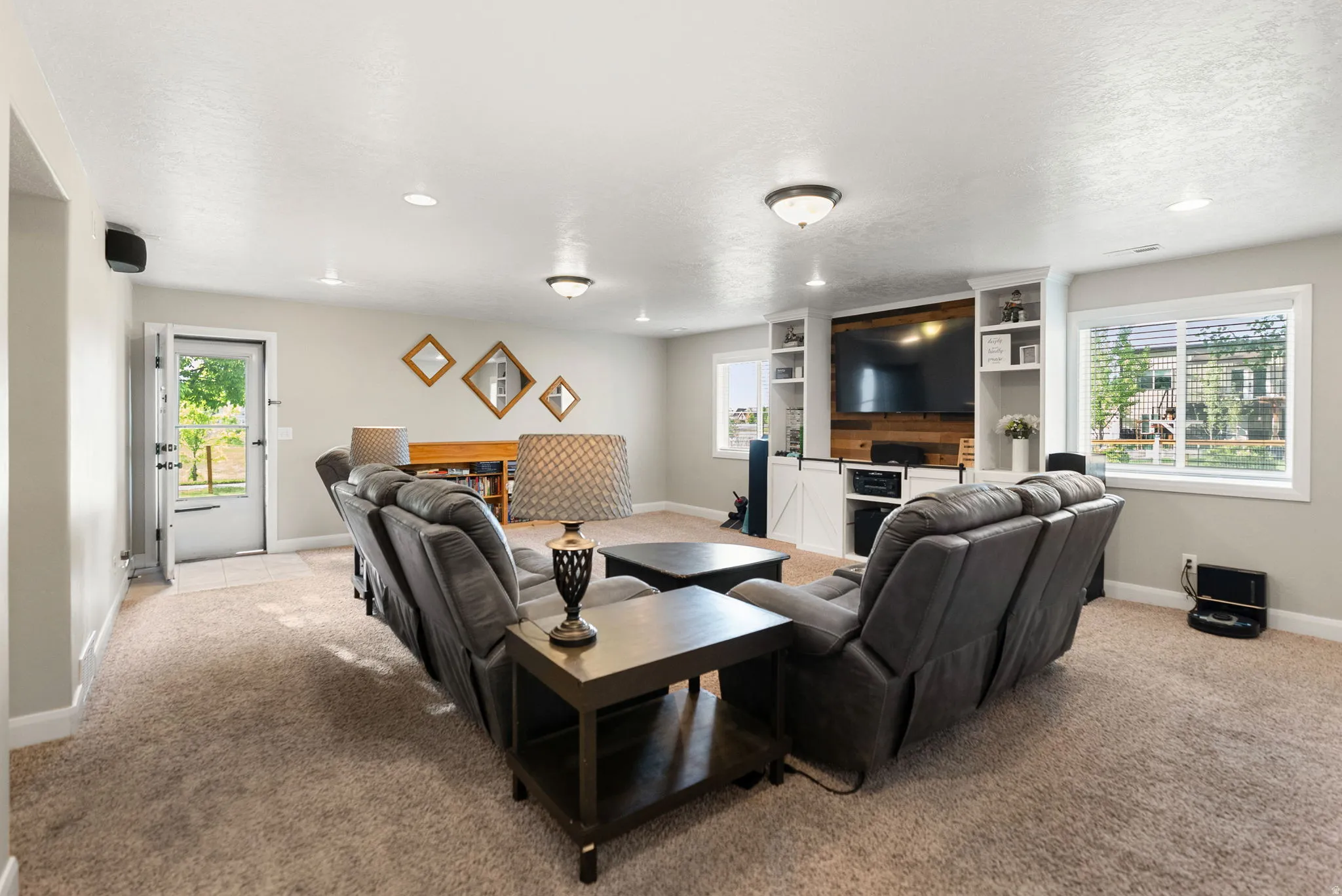 Spacious entertainment area featuring neutral-toned carpeting, recessed lighting, and a built-in media center with shelving