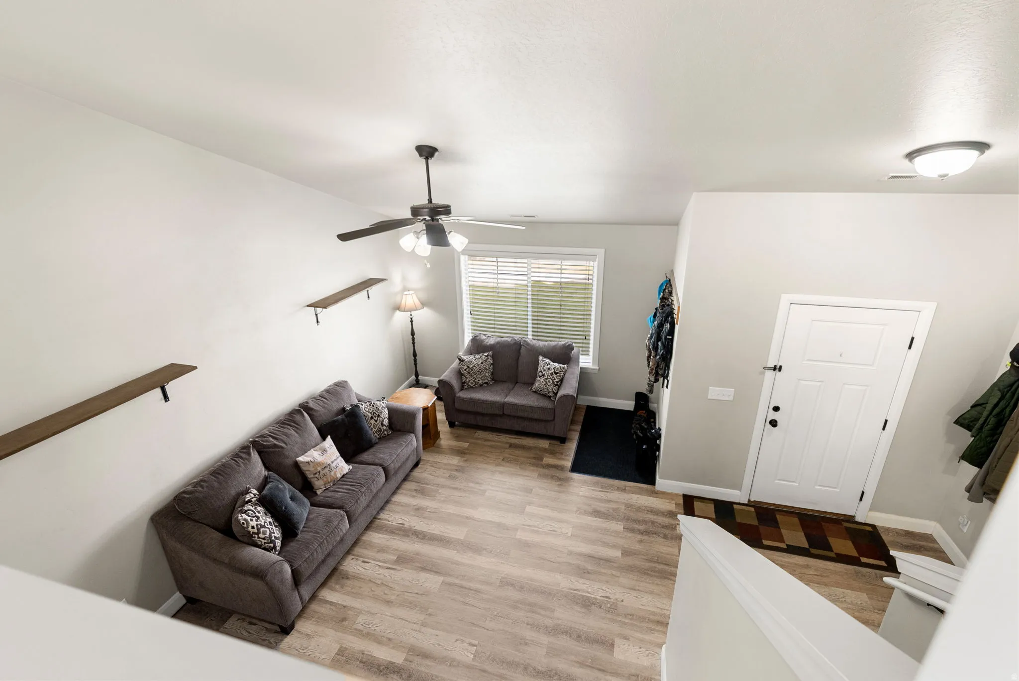 Open-concept living area featuring wood-finish flooring, a ceiling fan with integrated lighting, and high ceilings
