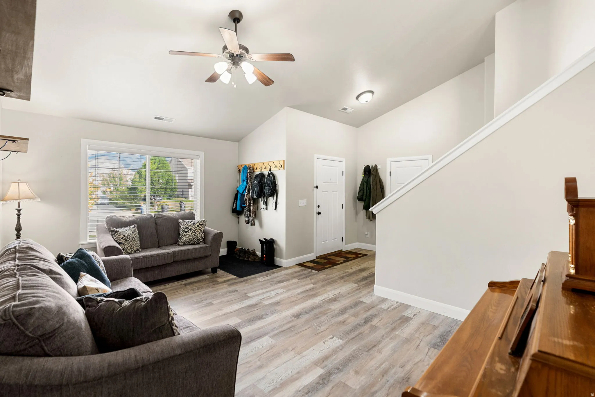 Spacious living area featuring light wood-finish flooring, vaulted ceilings, and a large window with blinds