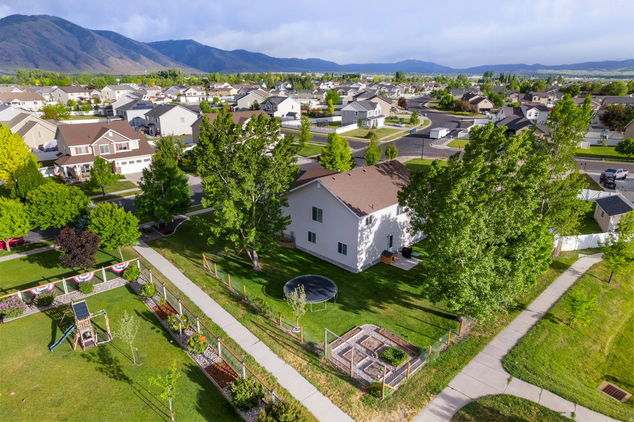 Corner lot property featuring a spacious grass yard, mature trees, and raised garden beds