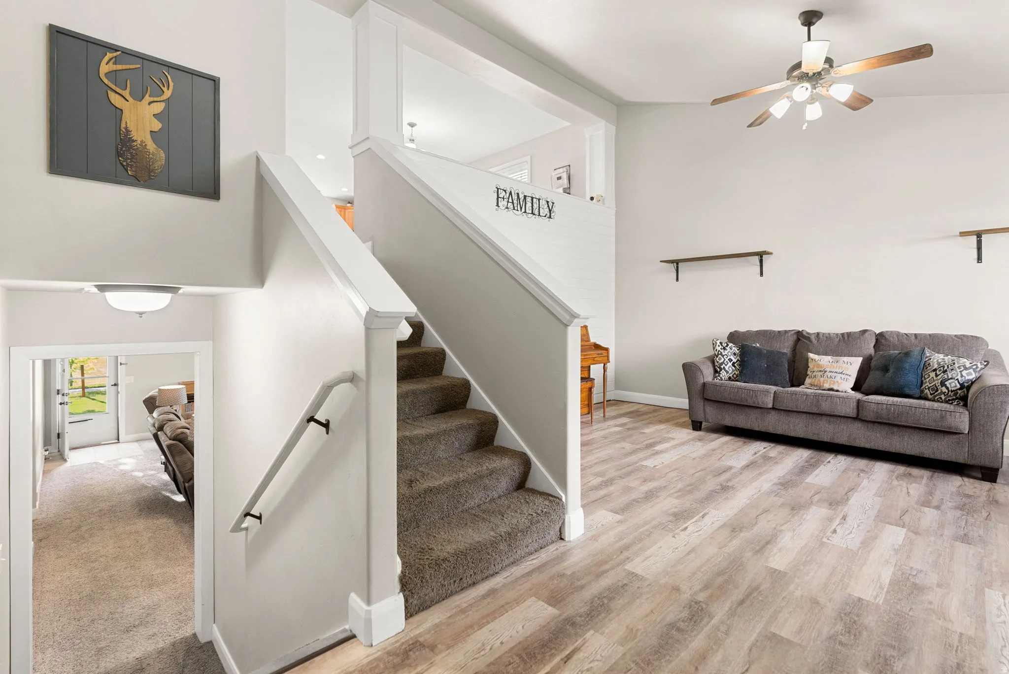 Open-concept living area featuring wood-finish flooring, a ceiling fan with integrated lighting, and a white staircase with carpeted treads