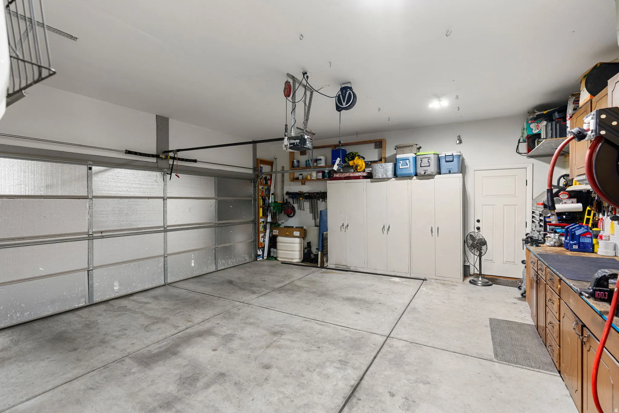 Spacious garage featuring a sectional garage door, concrete flooring, extensive built-in cabinetry, and a work bench with upper shelving