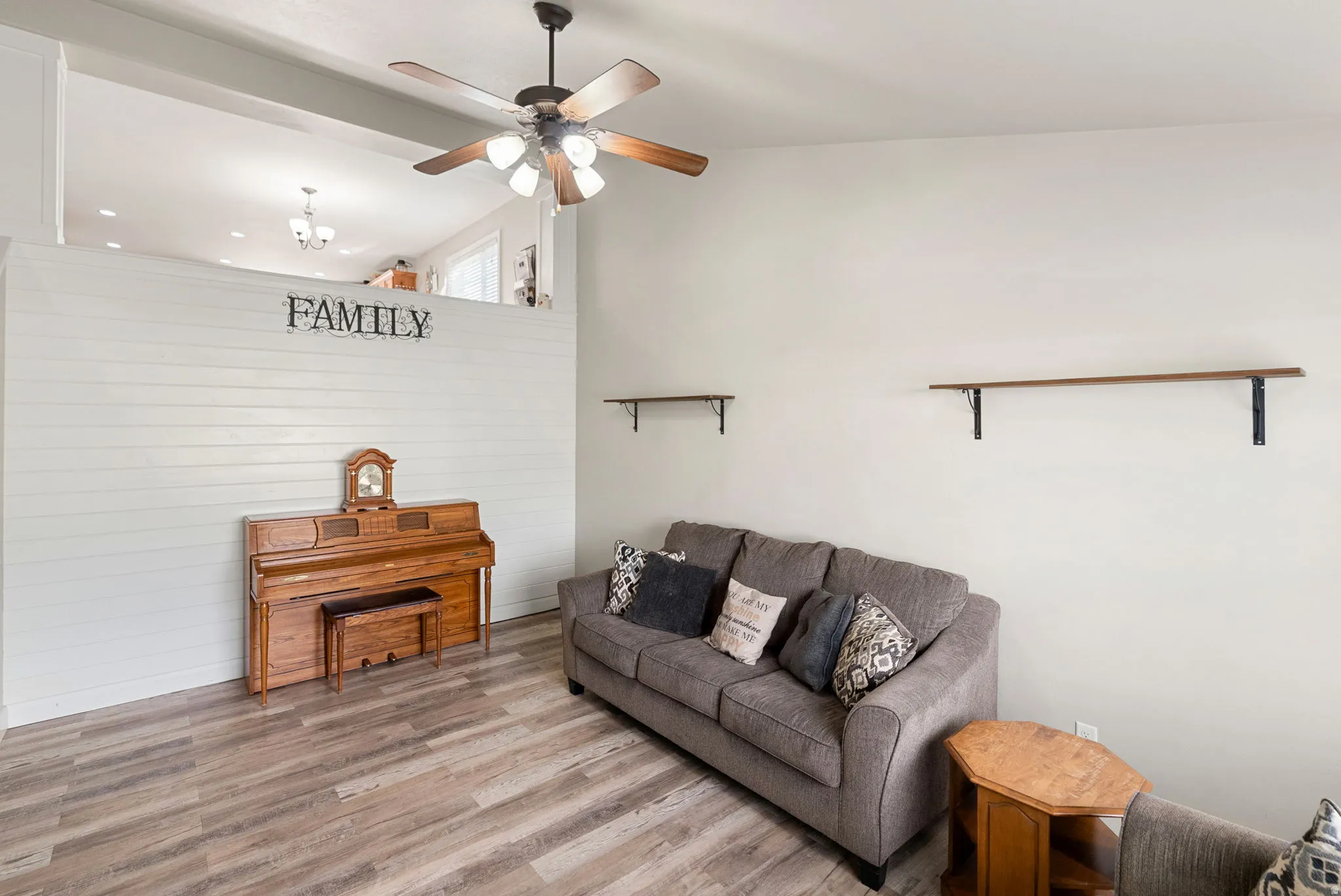 Spacious living area featuring wood-finish flooring, a white shiplap accent wall, and a ceiling fan with light fixture