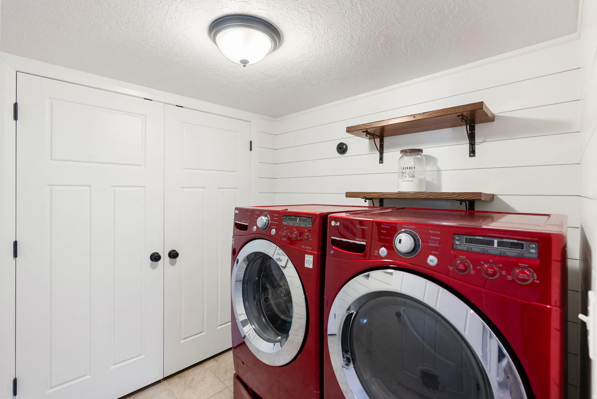 Laundry area featuring shiplap wall paneling, two-panel bifold doors, and wood-finish shelving with black metal brackets