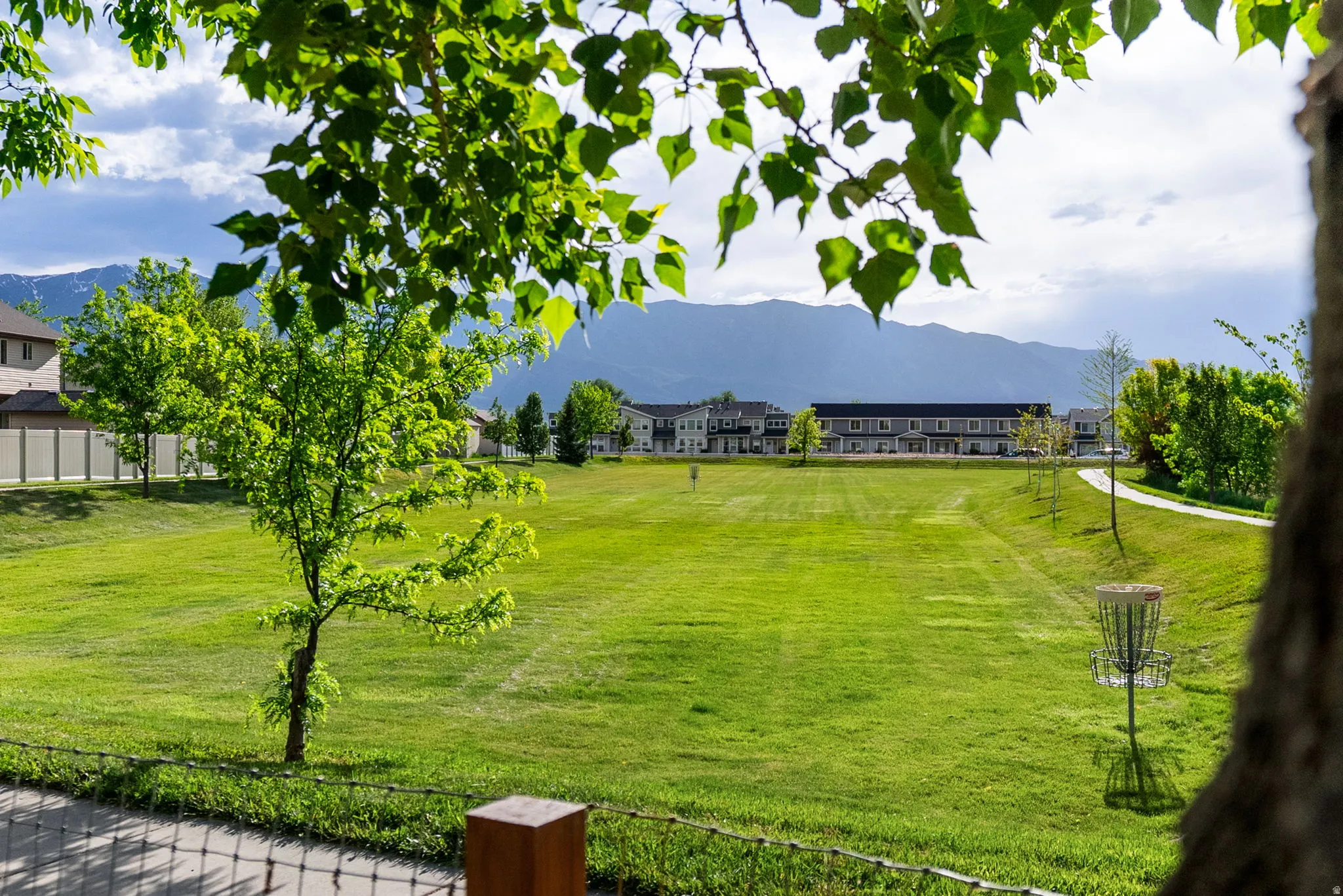 Expansive green space featuring a manicured lawn, established trees, and a paved pathway