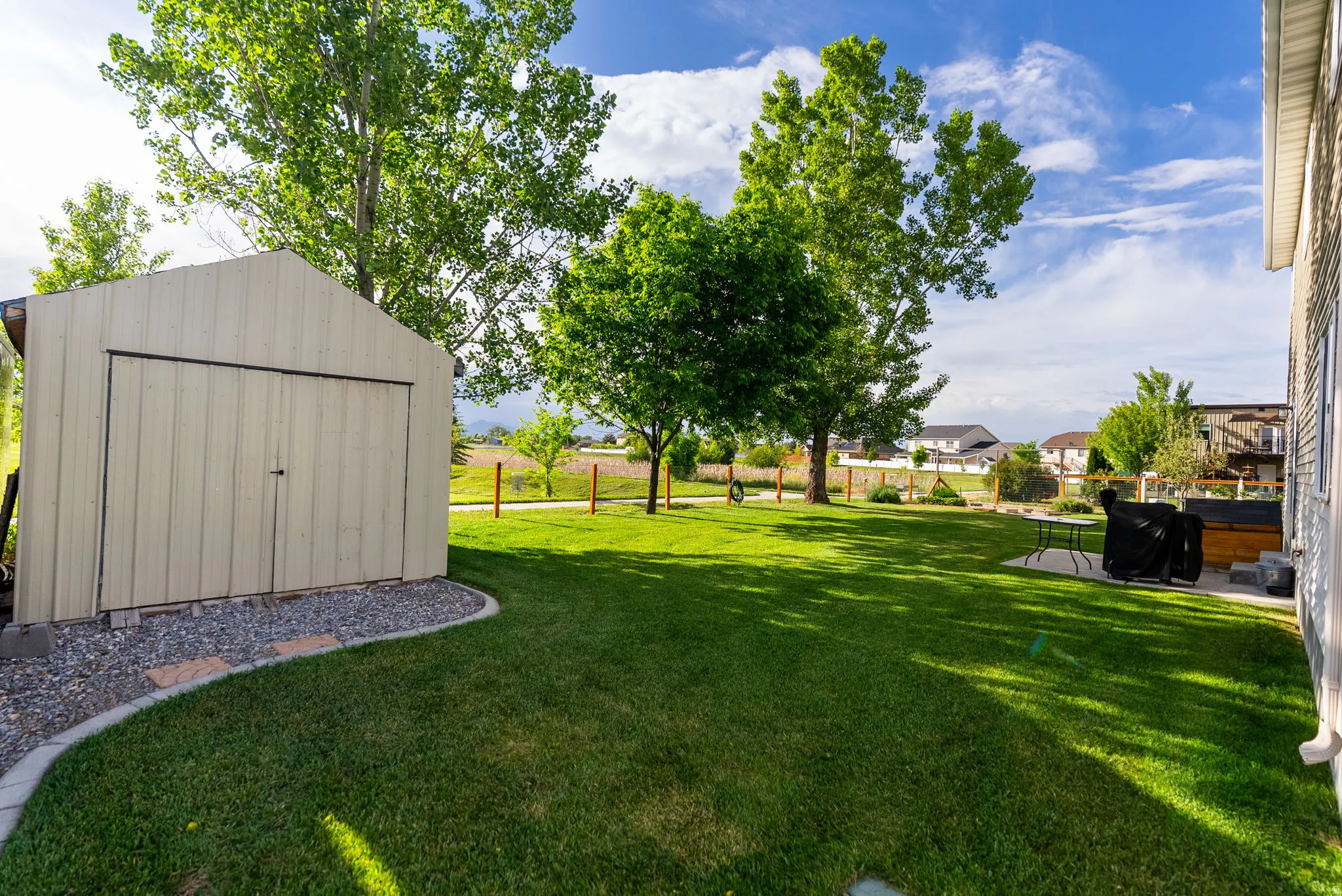 Expansive green lawn featuring a storage shed with double doors, bordered by a gravel and paver pathway