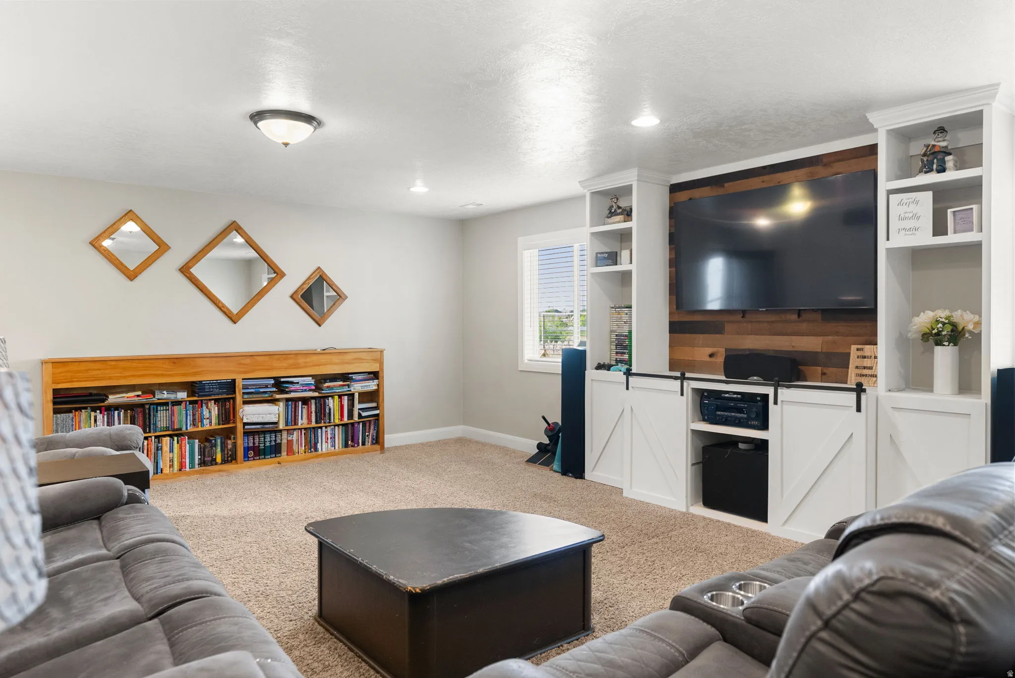 Entertainment area featuring built-in shelving, a wood accent wall, and white barn-door style cabinetry