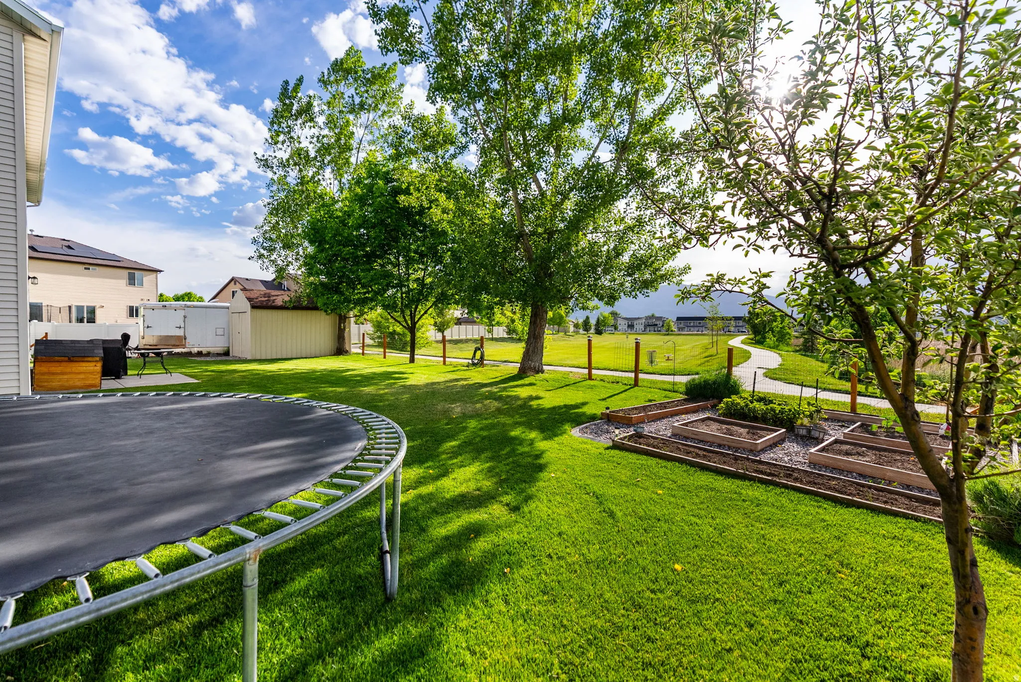 Expansive backyard featuring a manicured lawn, established trees, and multiple raised garden beds