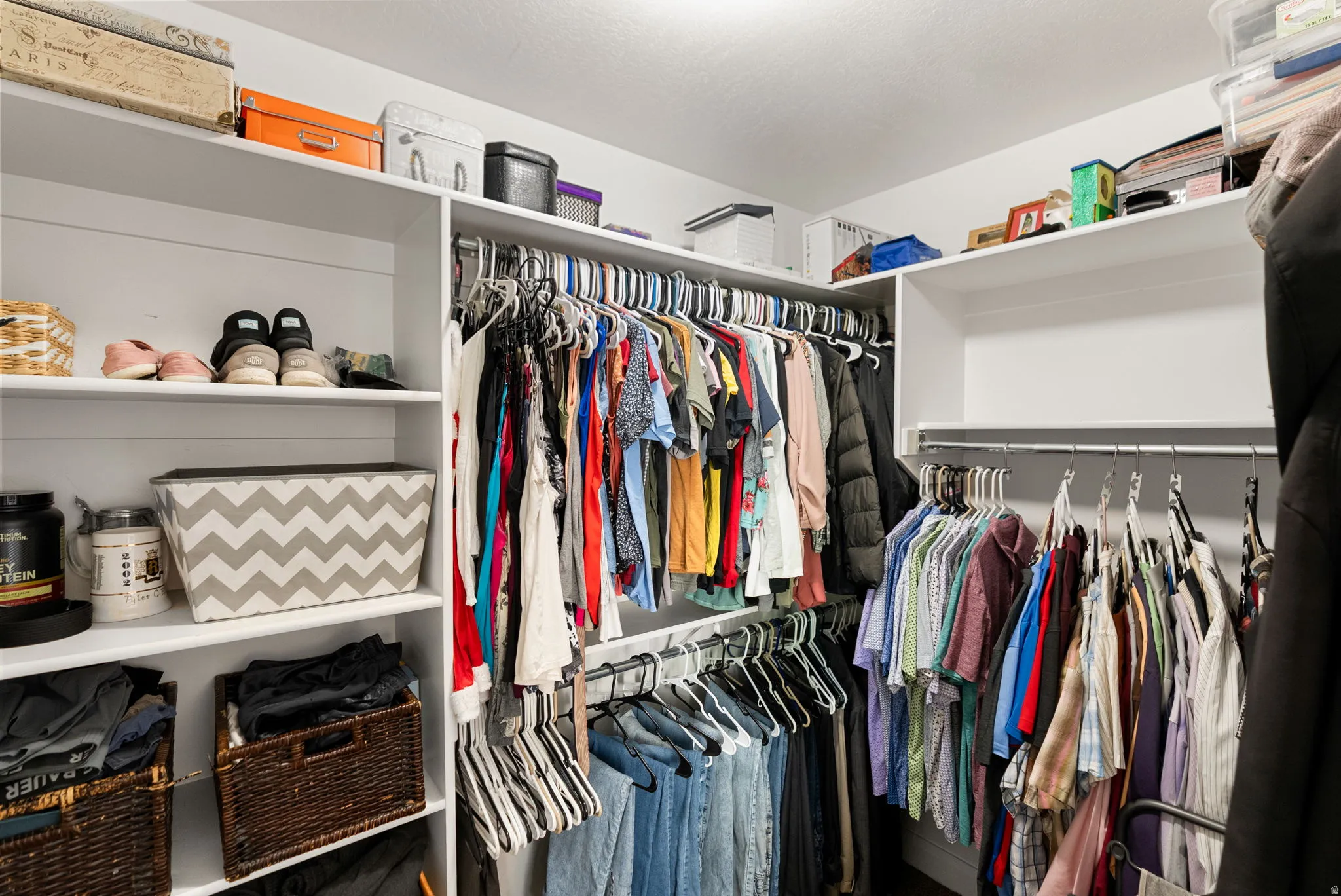 Expansive walk-in closet featuring white built-in shelving, multiple hanging rods for clothing organization, and high upper shelves for additional storage