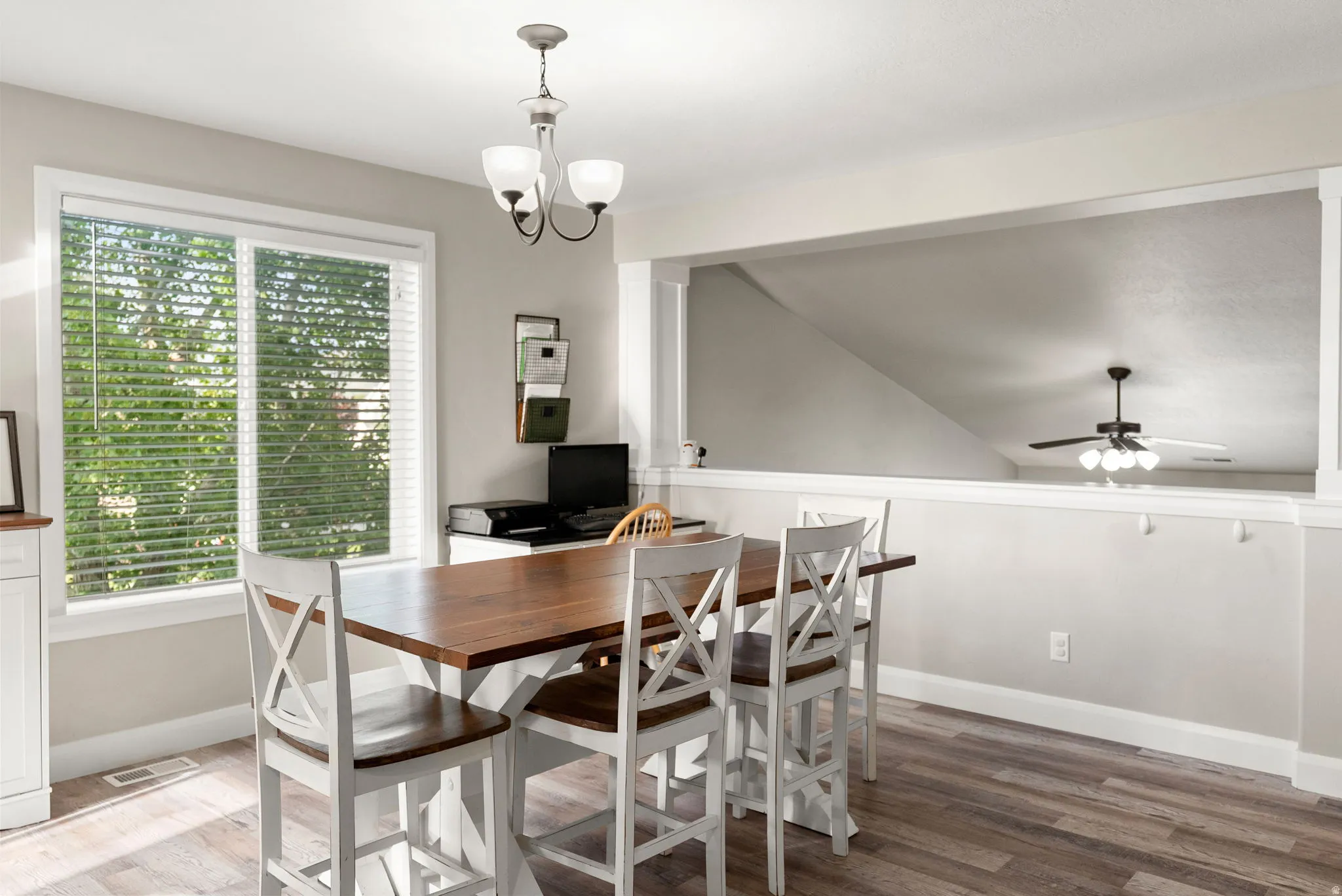 Dining area with wood-finish flooring, a large window with blinds, and a contemporary chandelier