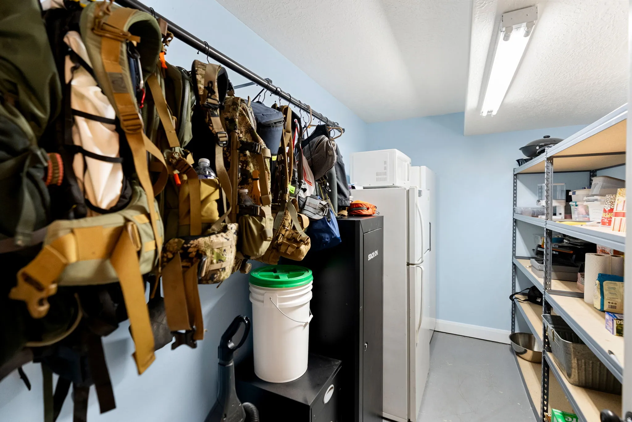 Dedicated storage area featuring expansive shelving units, two full-size refrigerators, and overhead fluorescent lighting