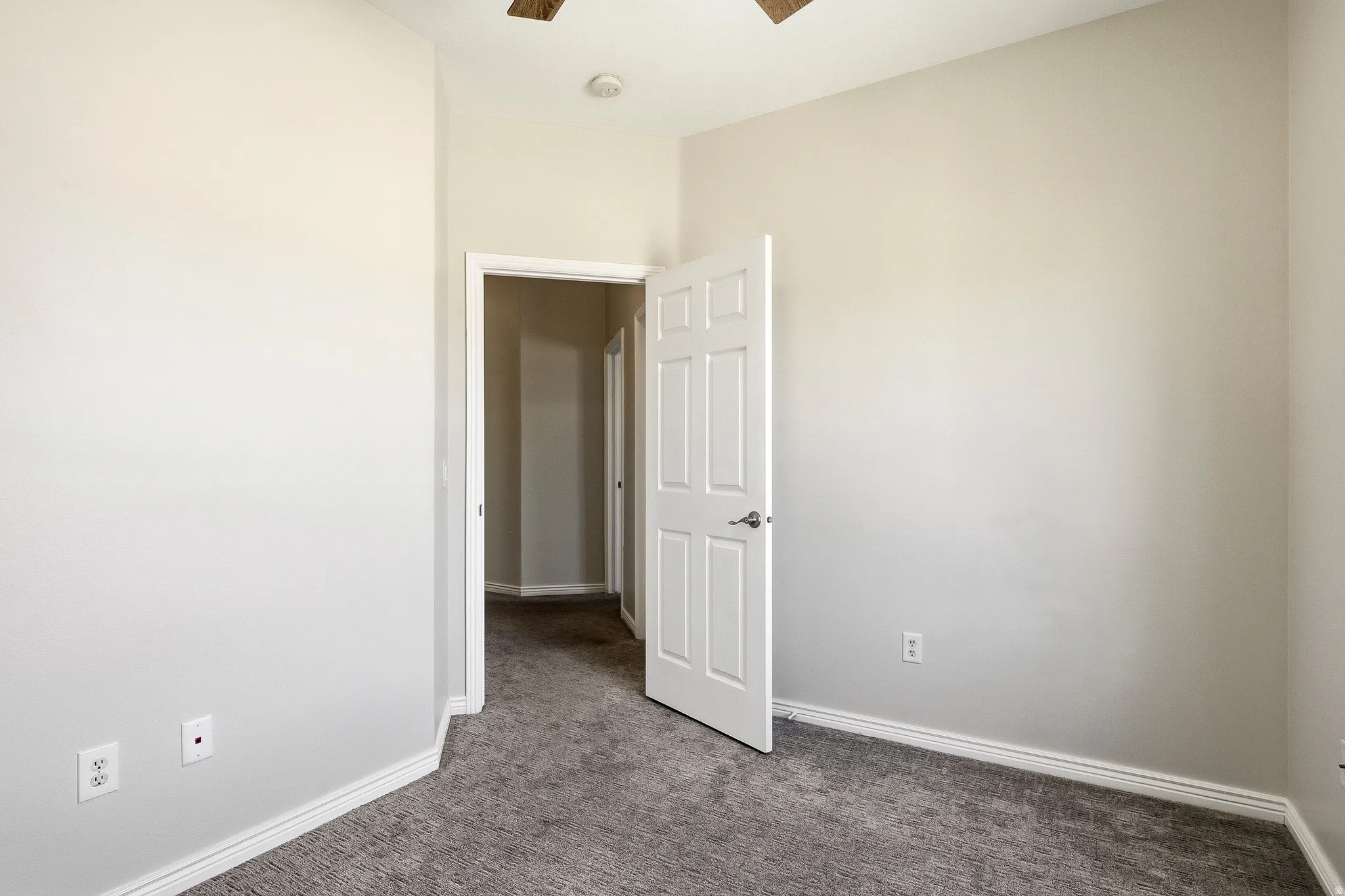 Interior room featuring neutral wall paint, gray patterned carpeting, white baseboards, and a white paneled door with silver hardware