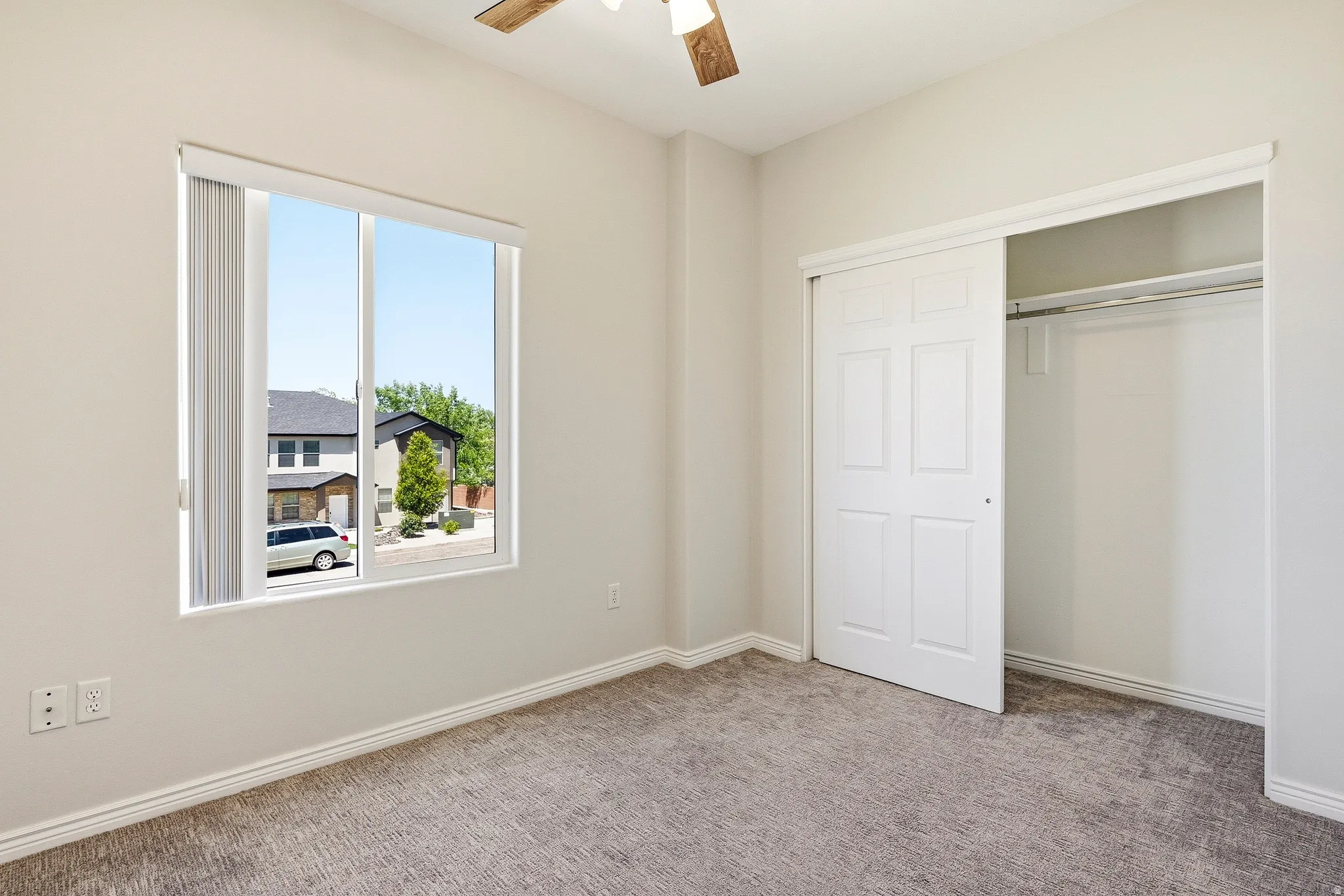 Bright room featuring light-colored carpet, a ceiling fan, and a large window with blinds