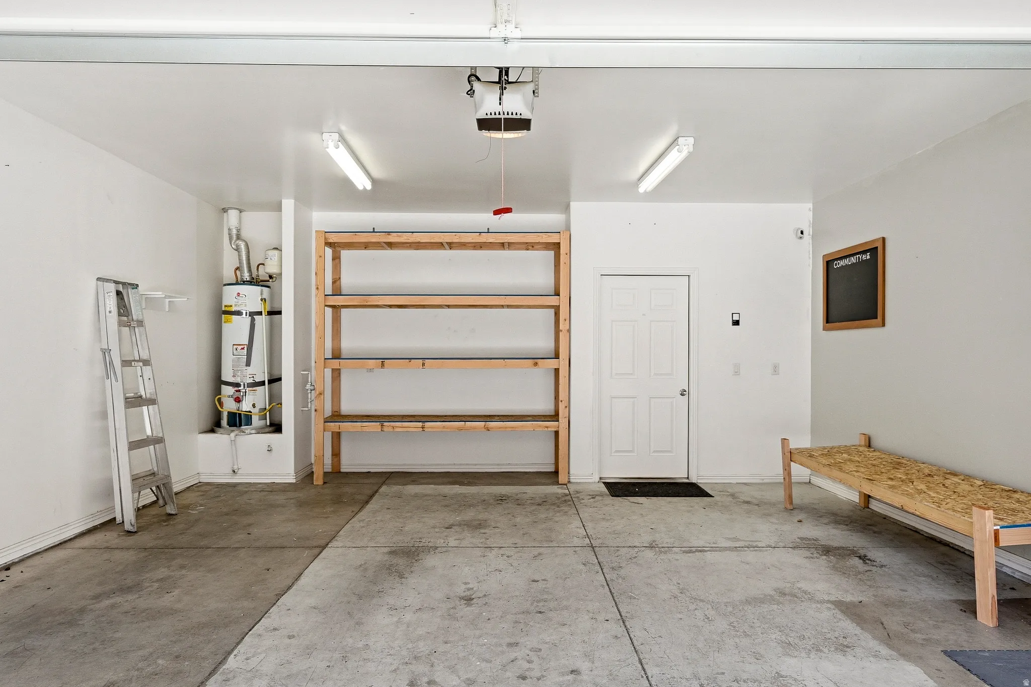 Spacious garage featuring concrete flooring, built-in wooden shelving, overhead lighting, and a paneled entry door