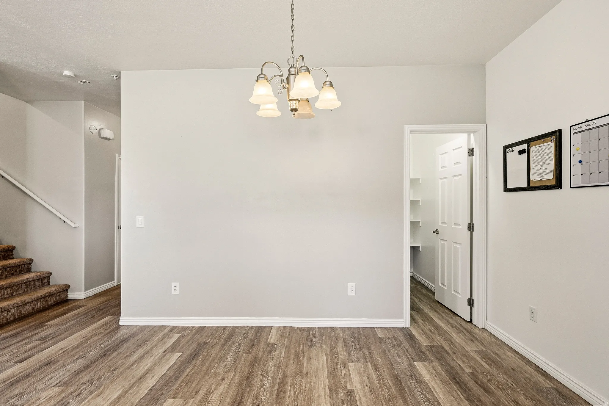 Open-concept area featuring wood-finish flooring, a contemporary chandelier, a pantry with shelving, white baseboards, and a neutral wall color