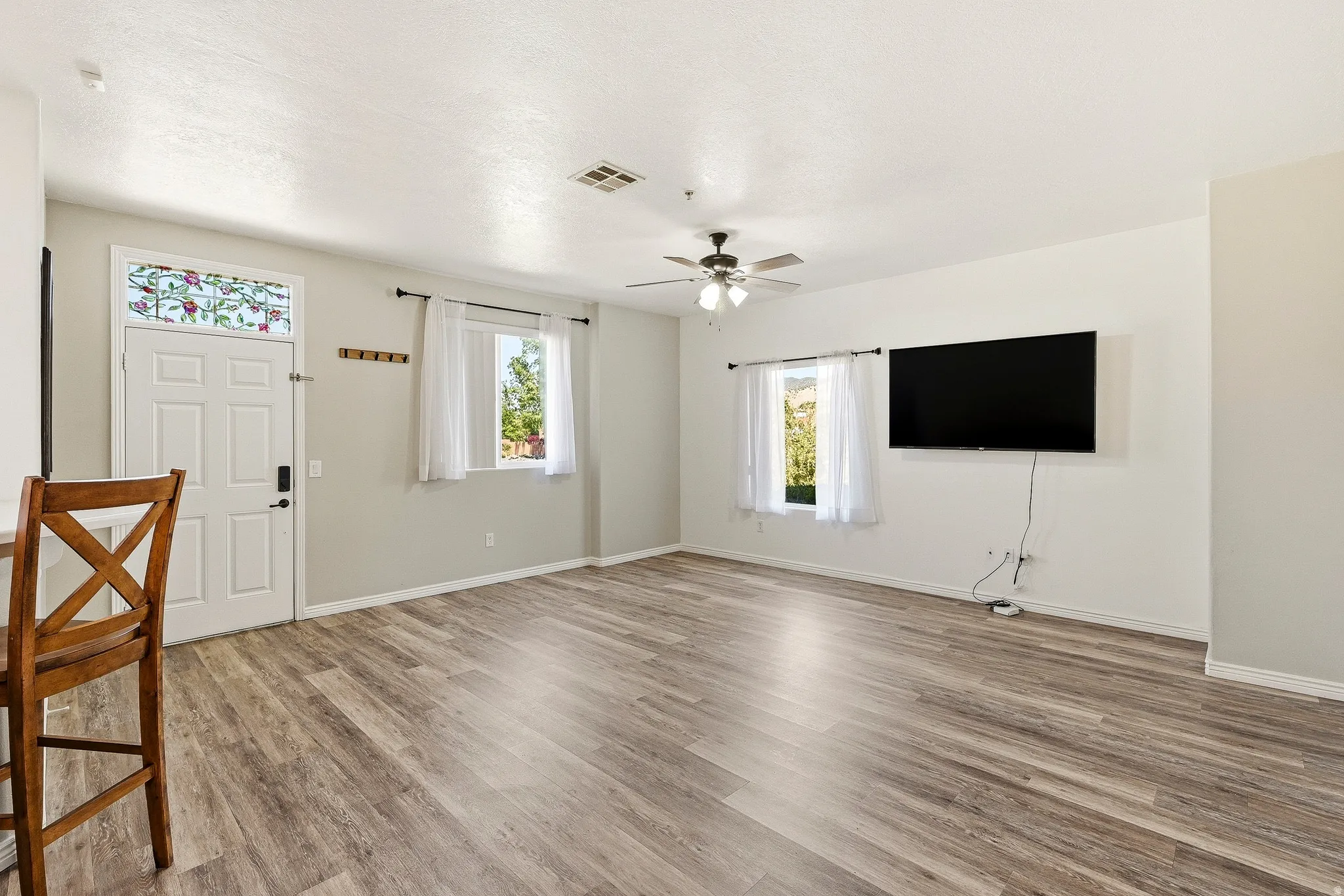 Spacious living area featuring wood-finish flooring, light gray wall paint, and multiple windows