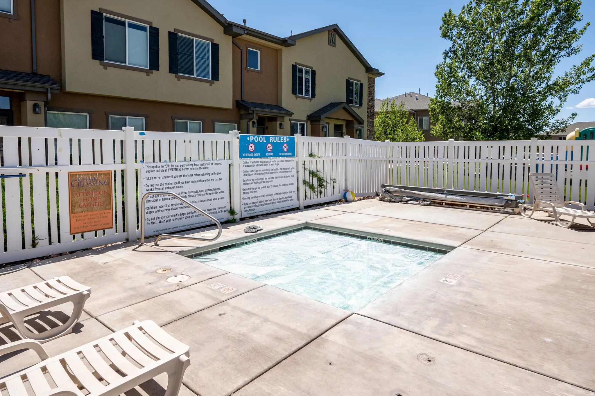 Outdoor spa featuring a concrete surround, white picket fencing, and surrounding residential structures