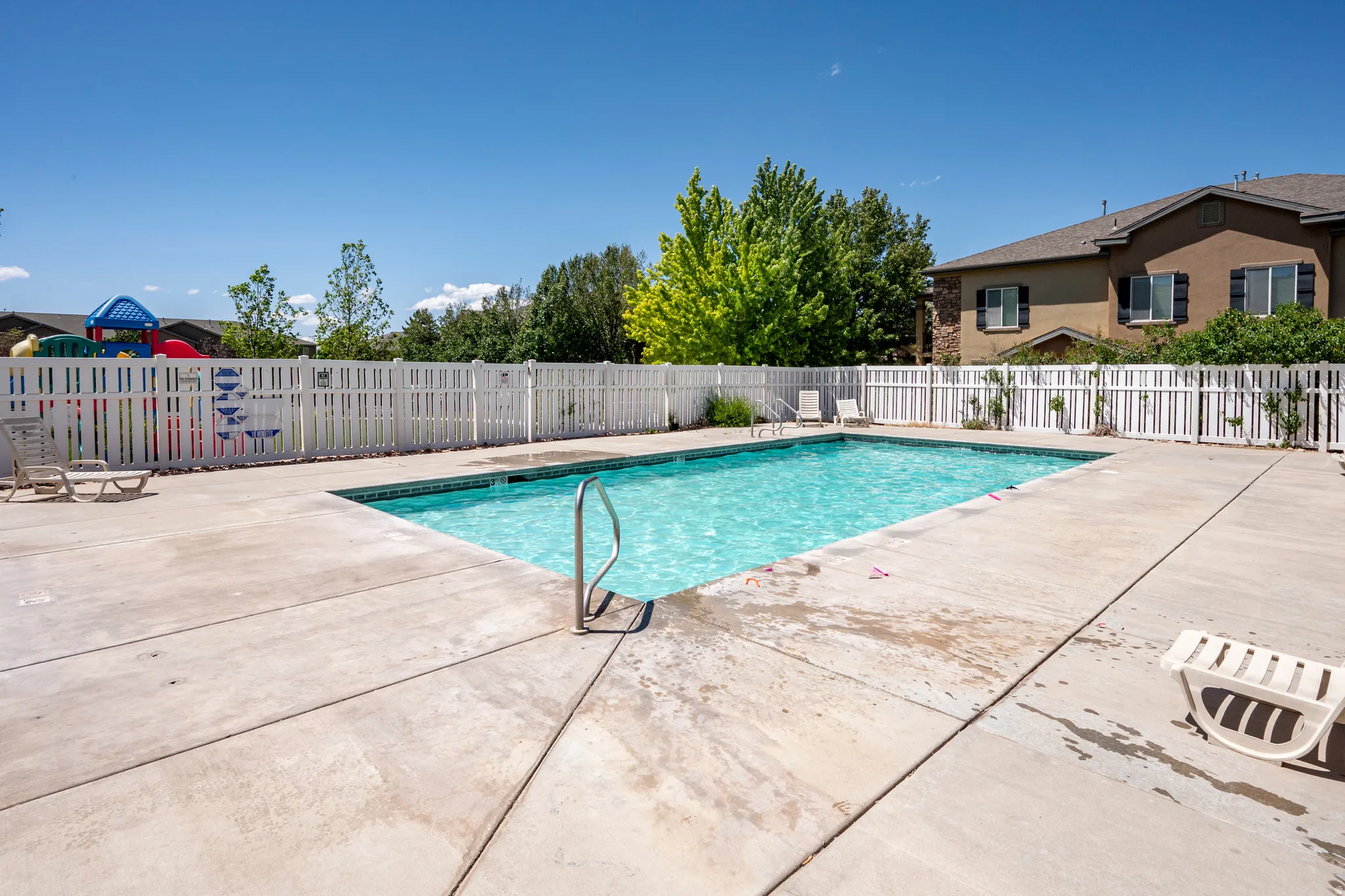 In-ground swimming pool with a concrete deck, surrounded by a white picket fence