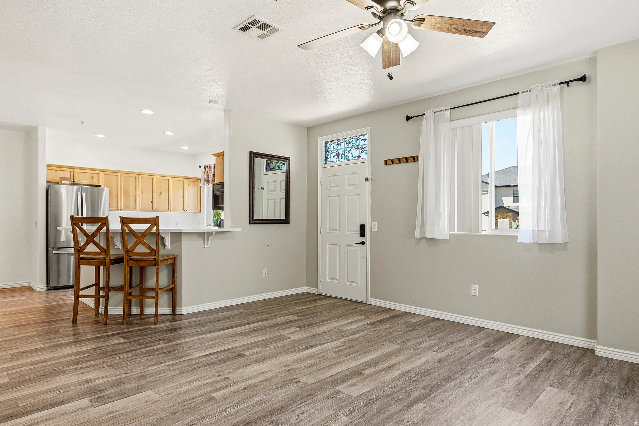 Open-concept living space featuring wood-finish flooring, a ceiling fan, and a front entry door with decorative glass