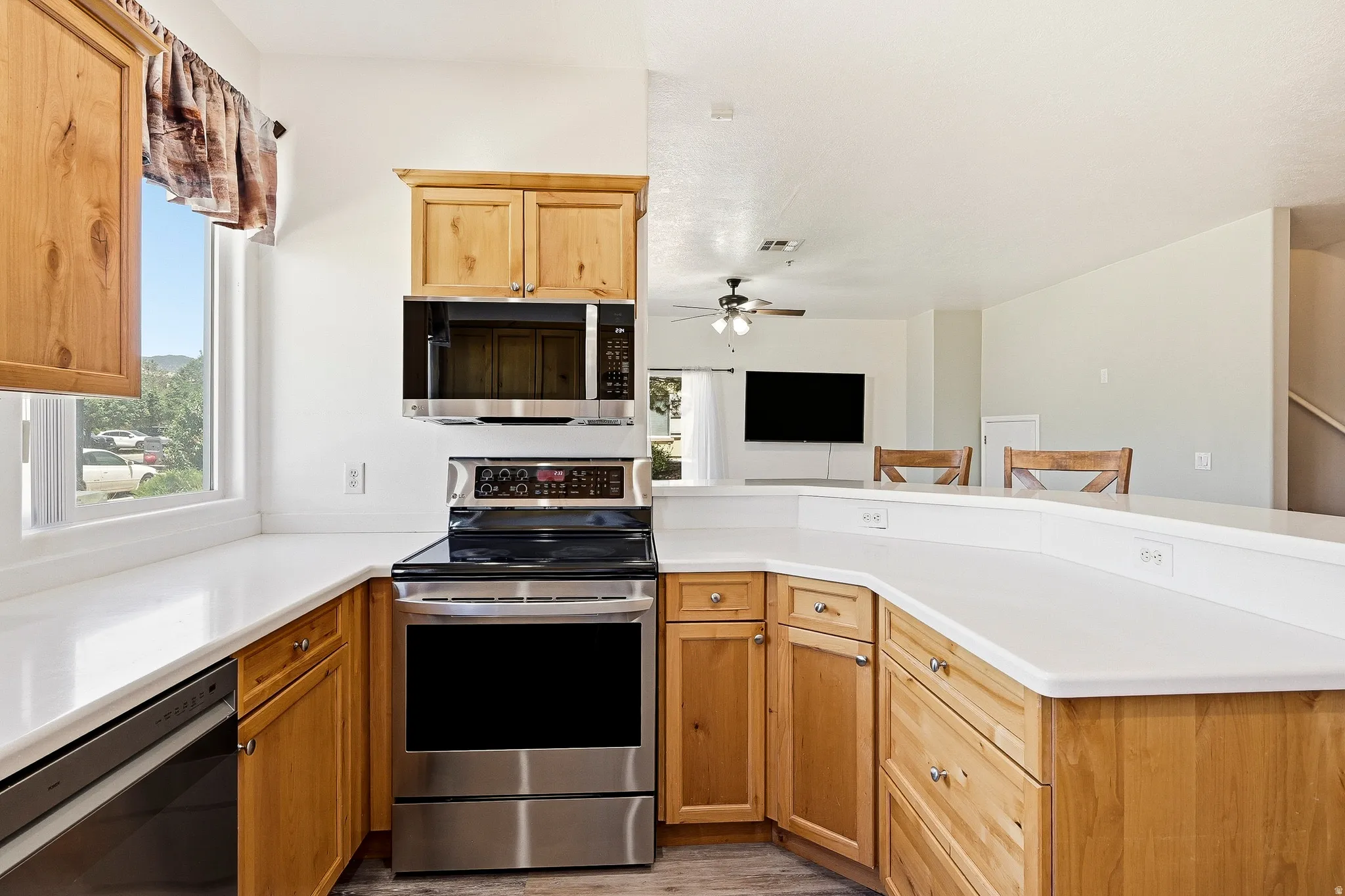 Kitchen featuring light wood cabinetry, white countertops, stainless steel appliances, and a window with outdoor scenery