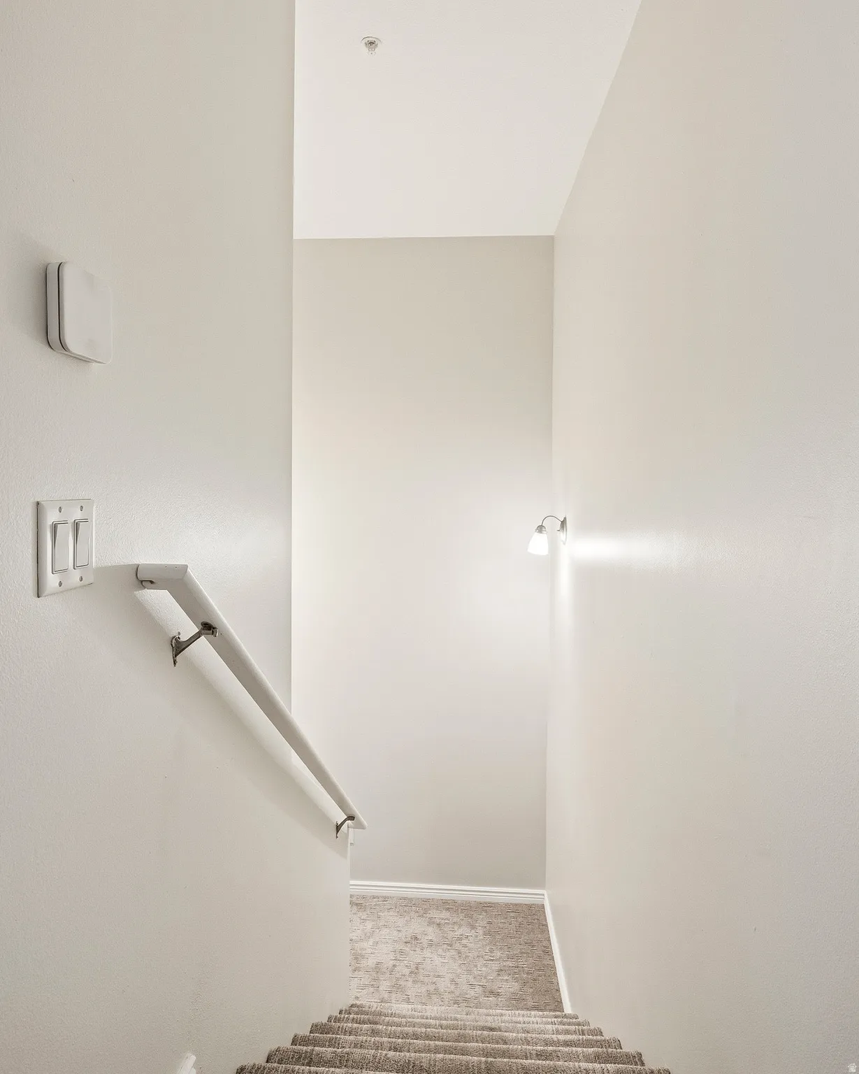 Carpeted staircase with a white handrail, illuminated by a wall-mounted sconce