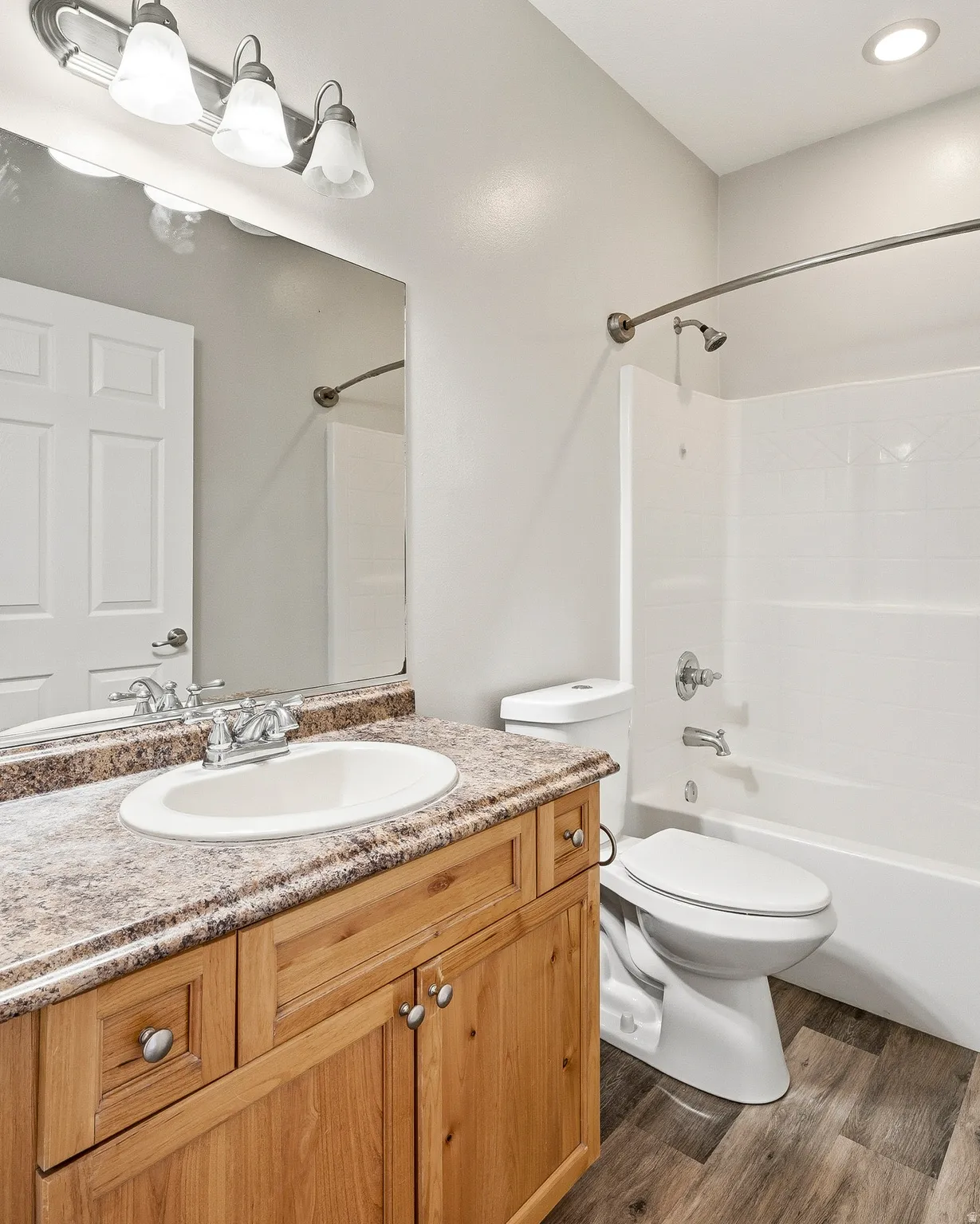Bathroom featuring a natural wood-finish vanity with a built-in sink, a speckled countertop, a large mirror, and a full bathtub with a shower