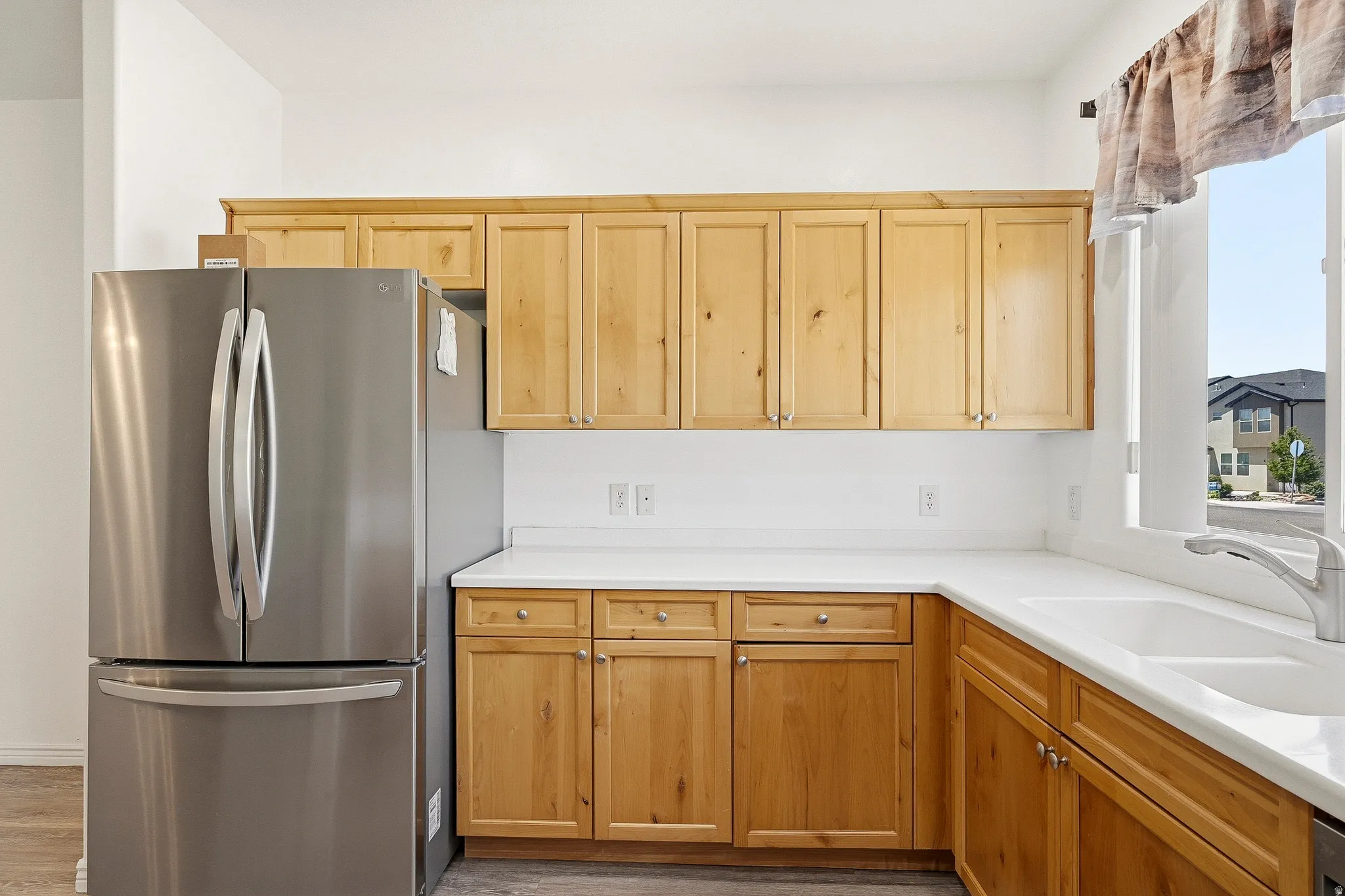 Kitchen featuring light wood cabinetry, white countertops, stainless steel French door refrigerator, and an undermount sink with a gooseneck faucet
