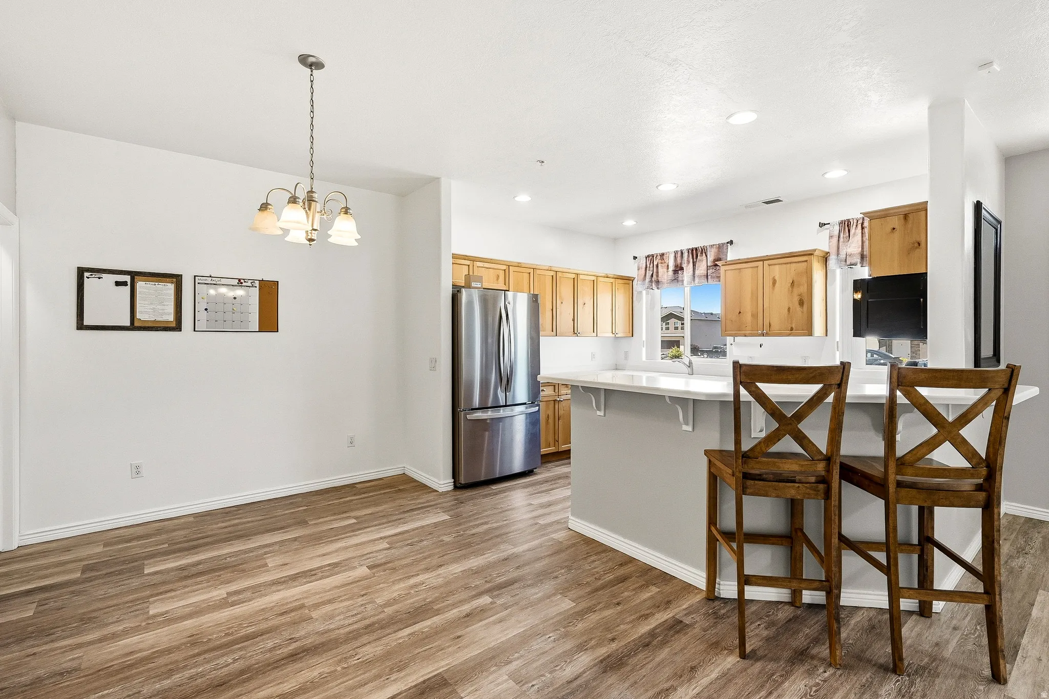 Open-concept dining area with wood-finish flooring, a contemporary chandelier, recessed lighting, and a breakfast bar with a solid surface countertop