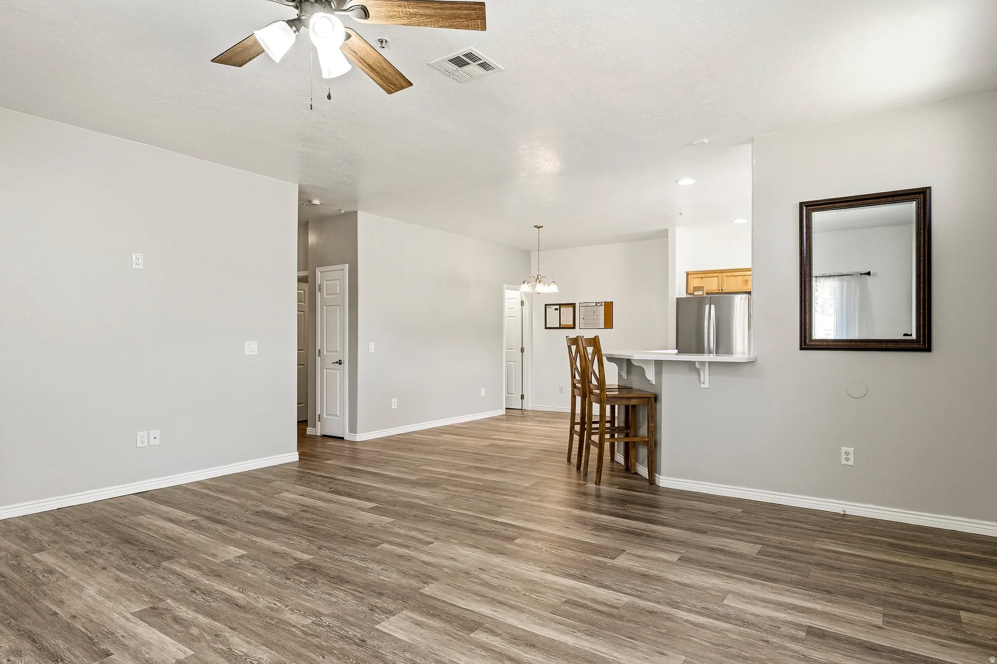 Open-concept living area featuring wood-finish flooring, a ceiling fan with light fixture, and neutral wall tones
