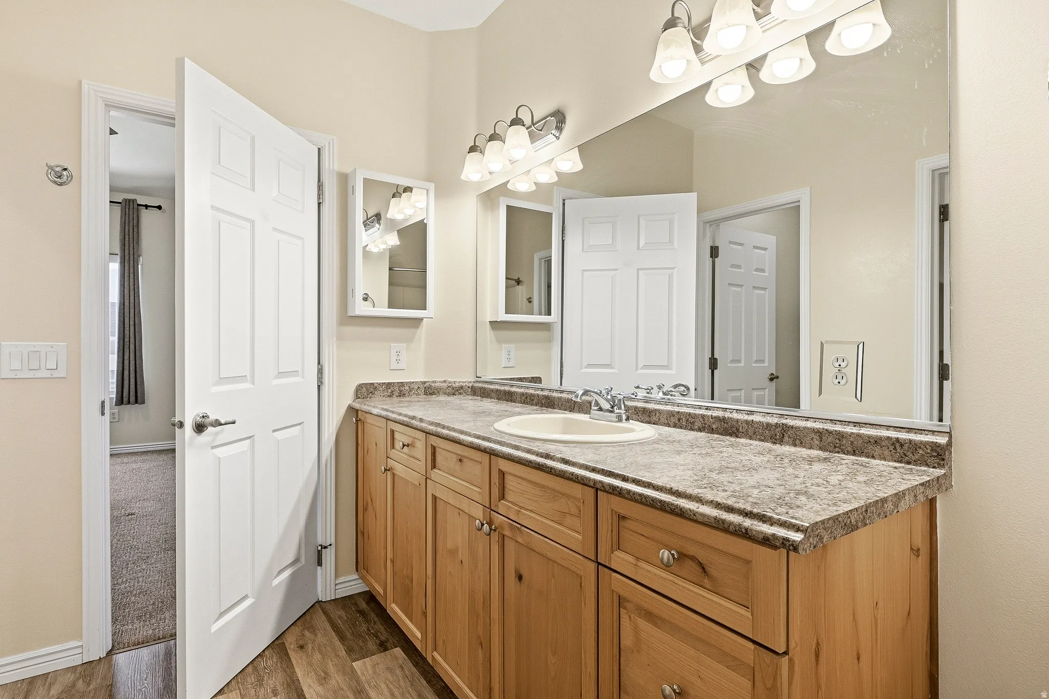 Bathroom featuring a wood-finish double vanity with a light speckled countertop, dual under-mount sinks, and a full-width mirror