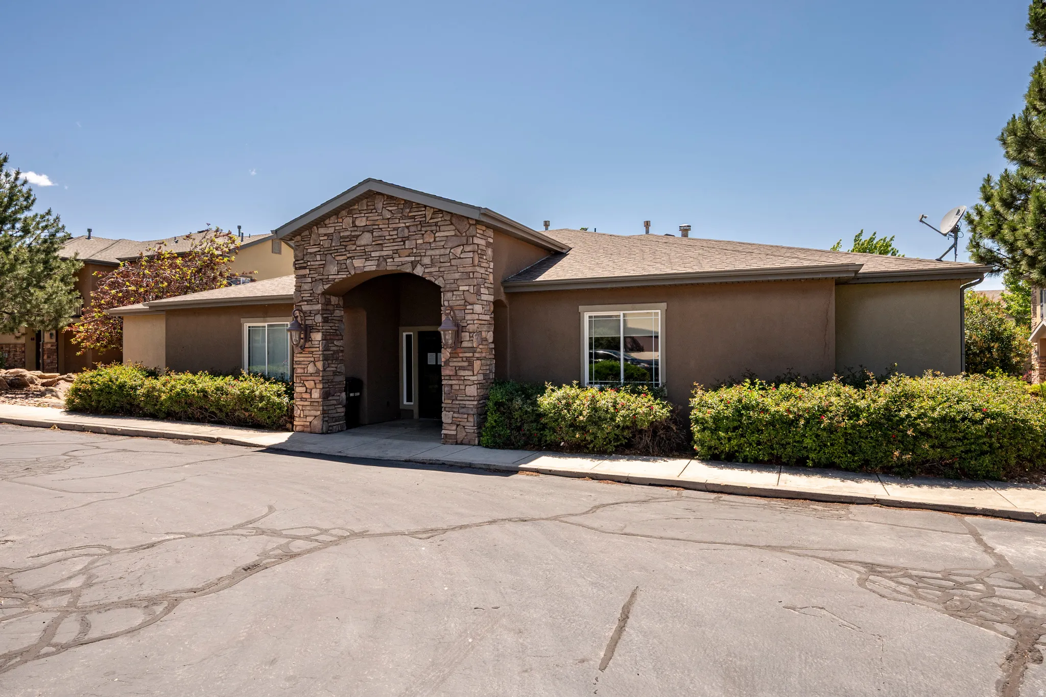Stucco exterior building featuring a stone veneer arched entrance, mature shrubbery, and a paved lot