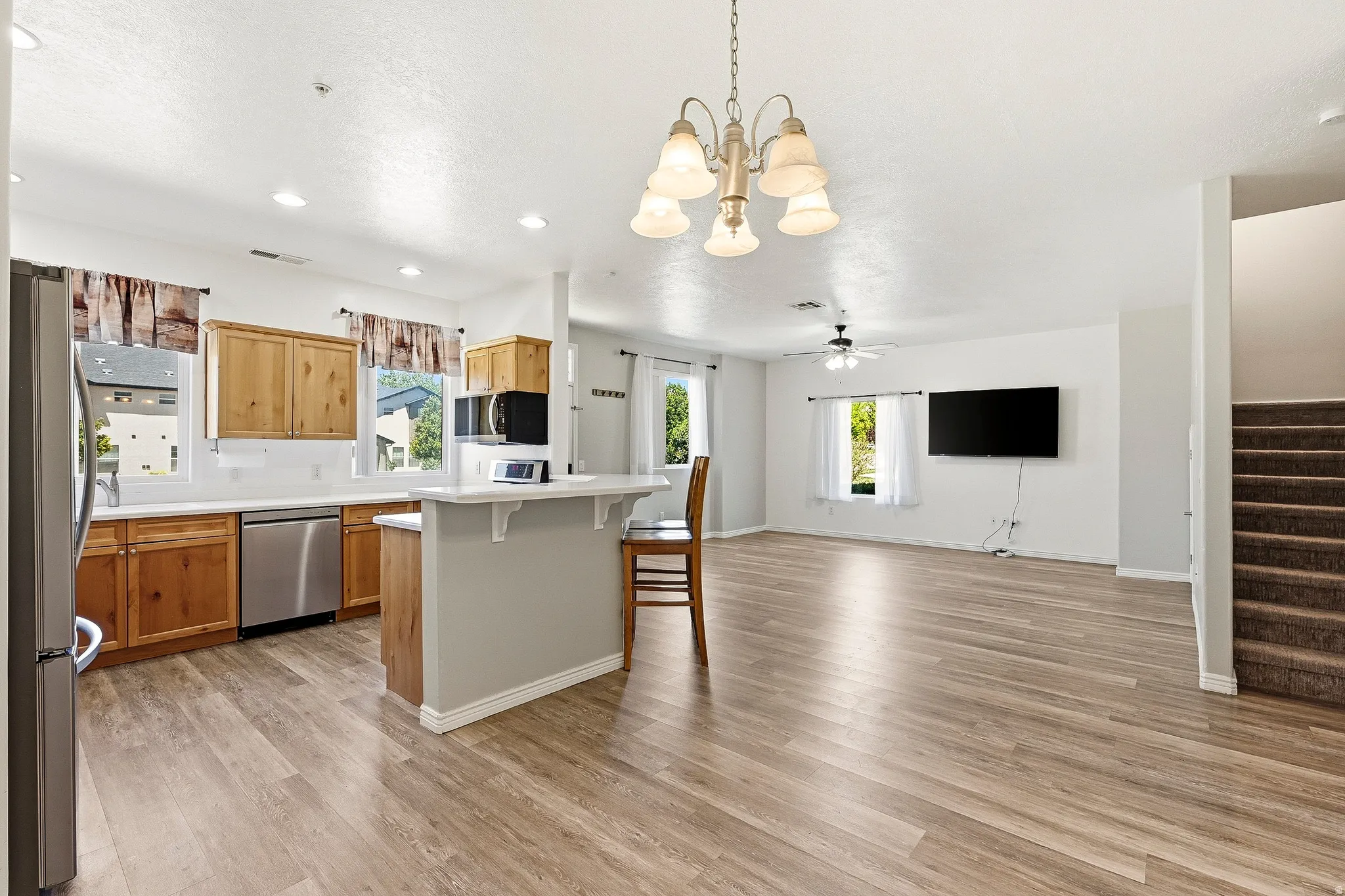 Open-concept living area featuring wood-finish flooring, a kitchen island with seating, stainless steel appliances, and natural wood cabinetry
