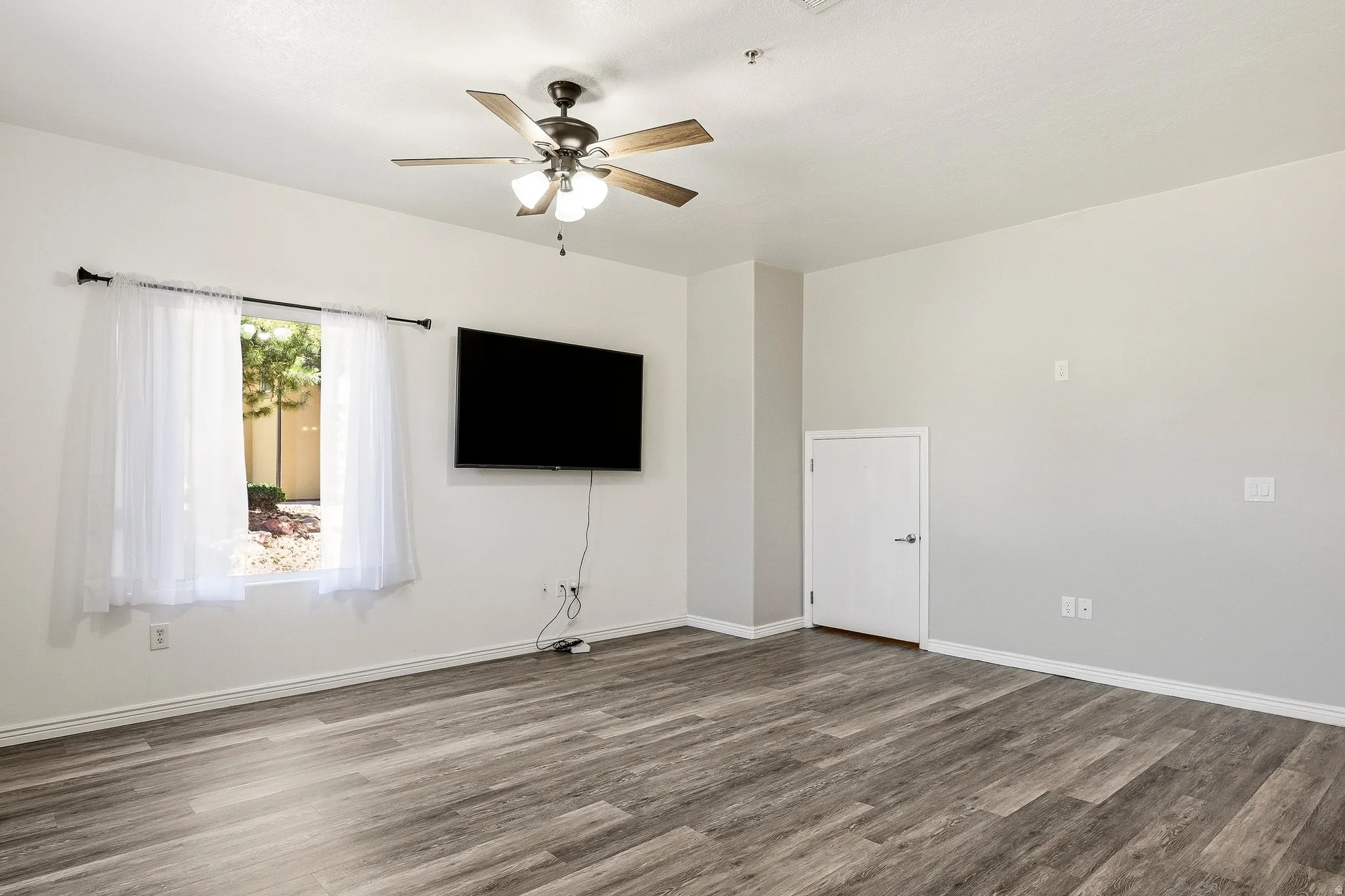 Spacious room featuring wood-finish flooring, a contemporary ceiling fan, and ample natural light from a large window