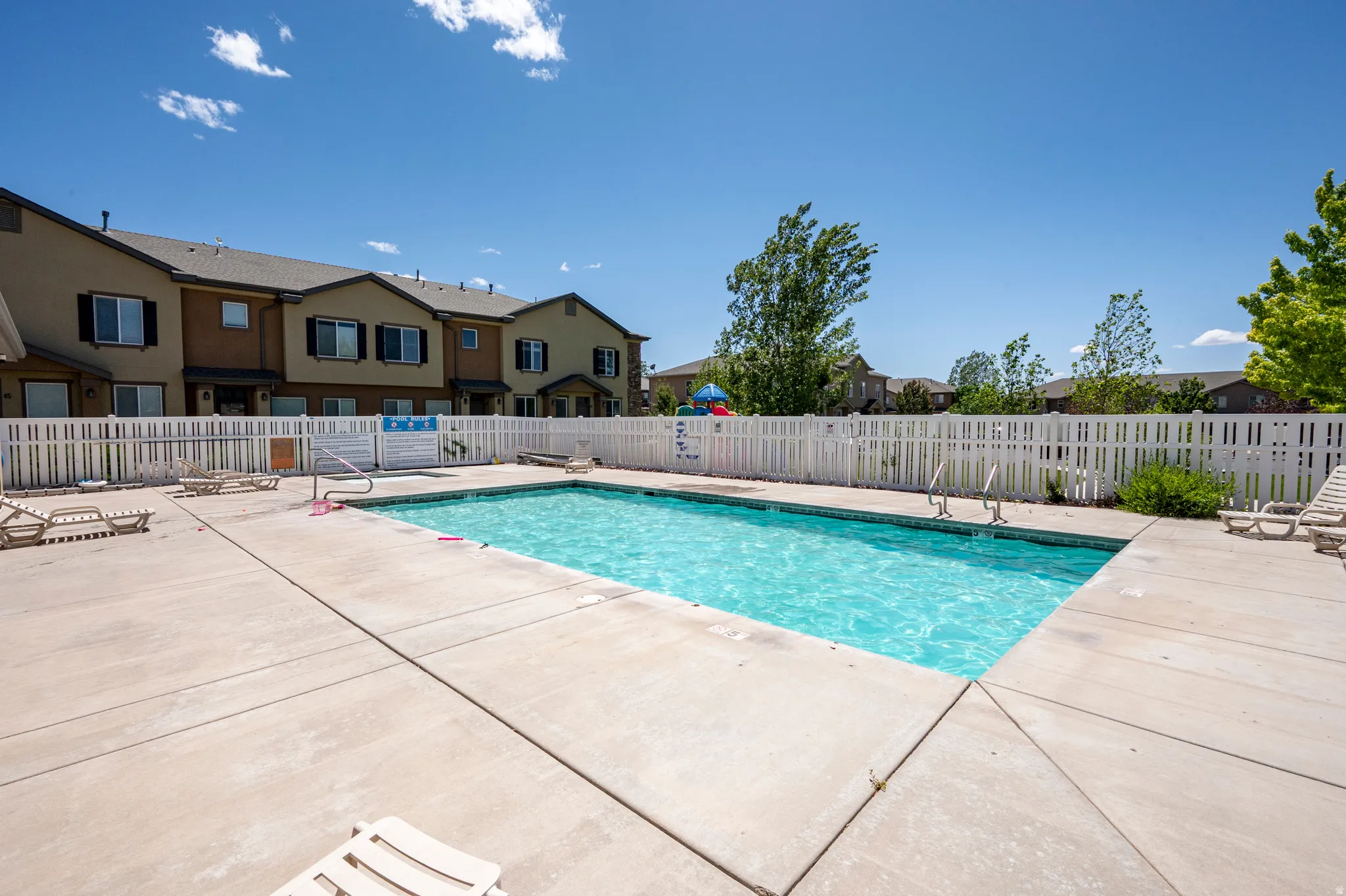 Rectangular swimming pool surrounded by a concrete deck and white picket fencing