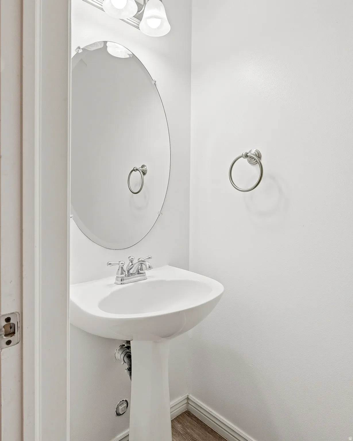Pedestal sink with chrome faucet, oval mirror, and wall-mounted light fixture