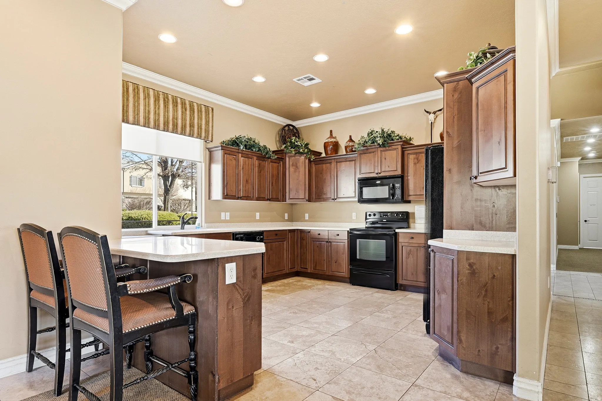 Well-appointed kitchen featuring abundant wood cabinetry, light-toned countertops, integrated black appliances, and recessed lighting