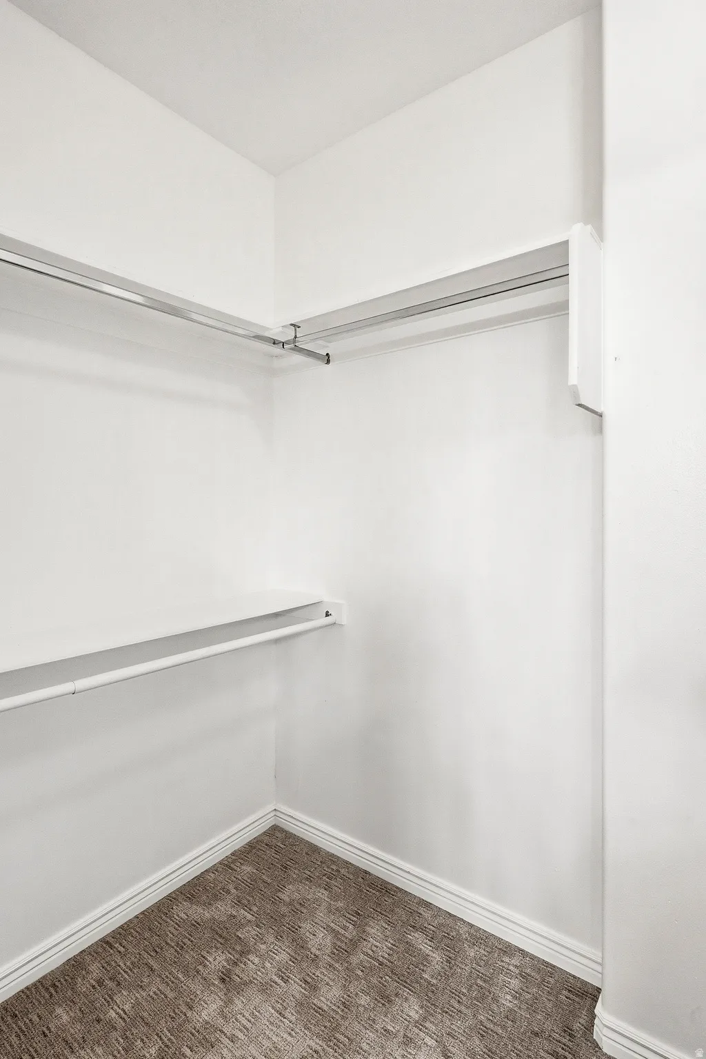 Walk-in closet featuring white walls, white baseboards, and patterned carpet flooring
