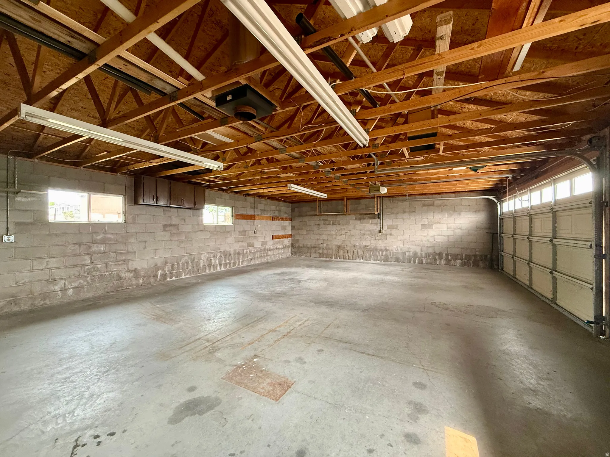 Spacious garage featuring concrete block walls, exposed wood ceiling joists, and a concrete floor