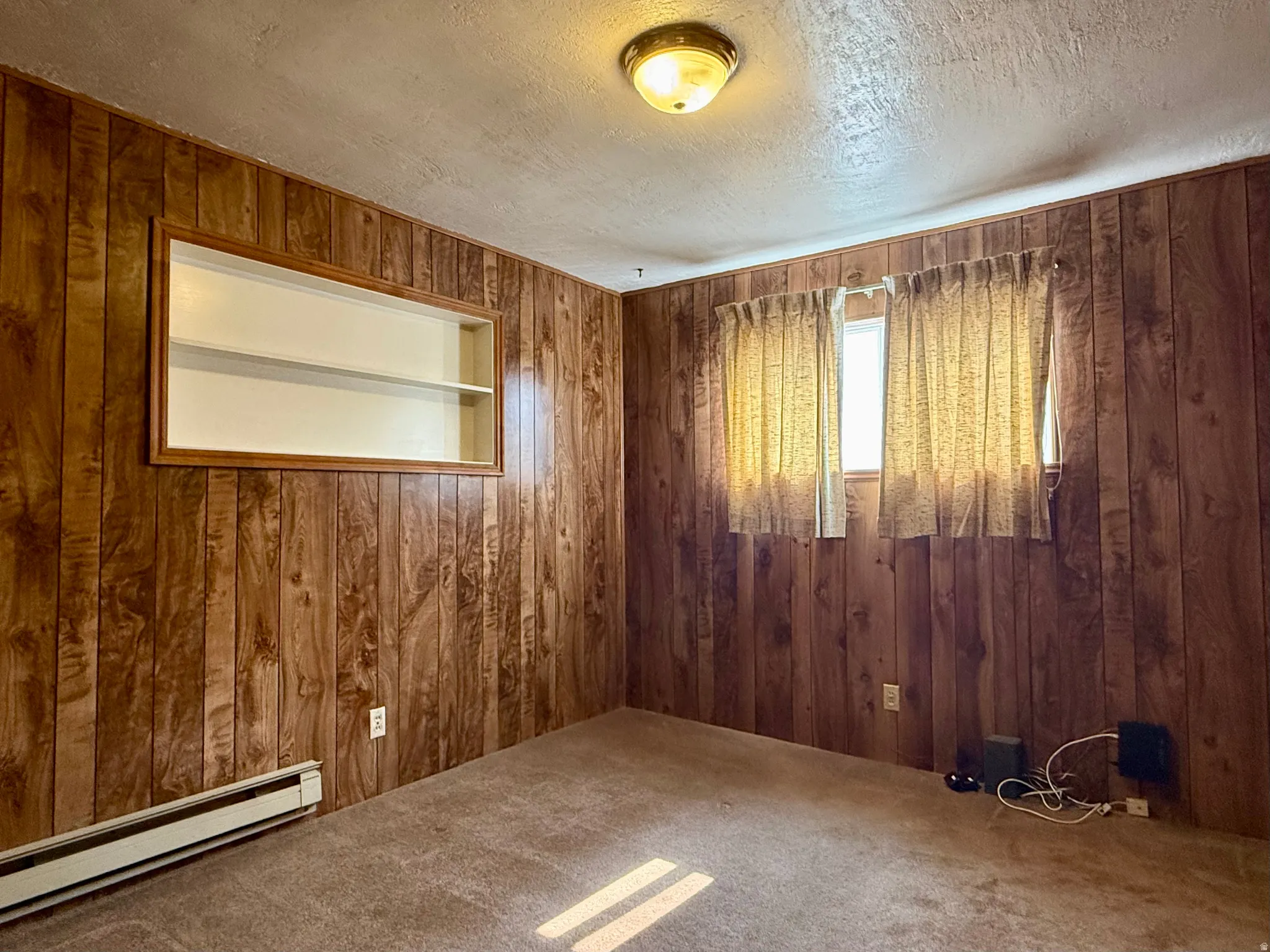 Room featuring wood-paneled walls, a built-in recessed shelf unit, and a window