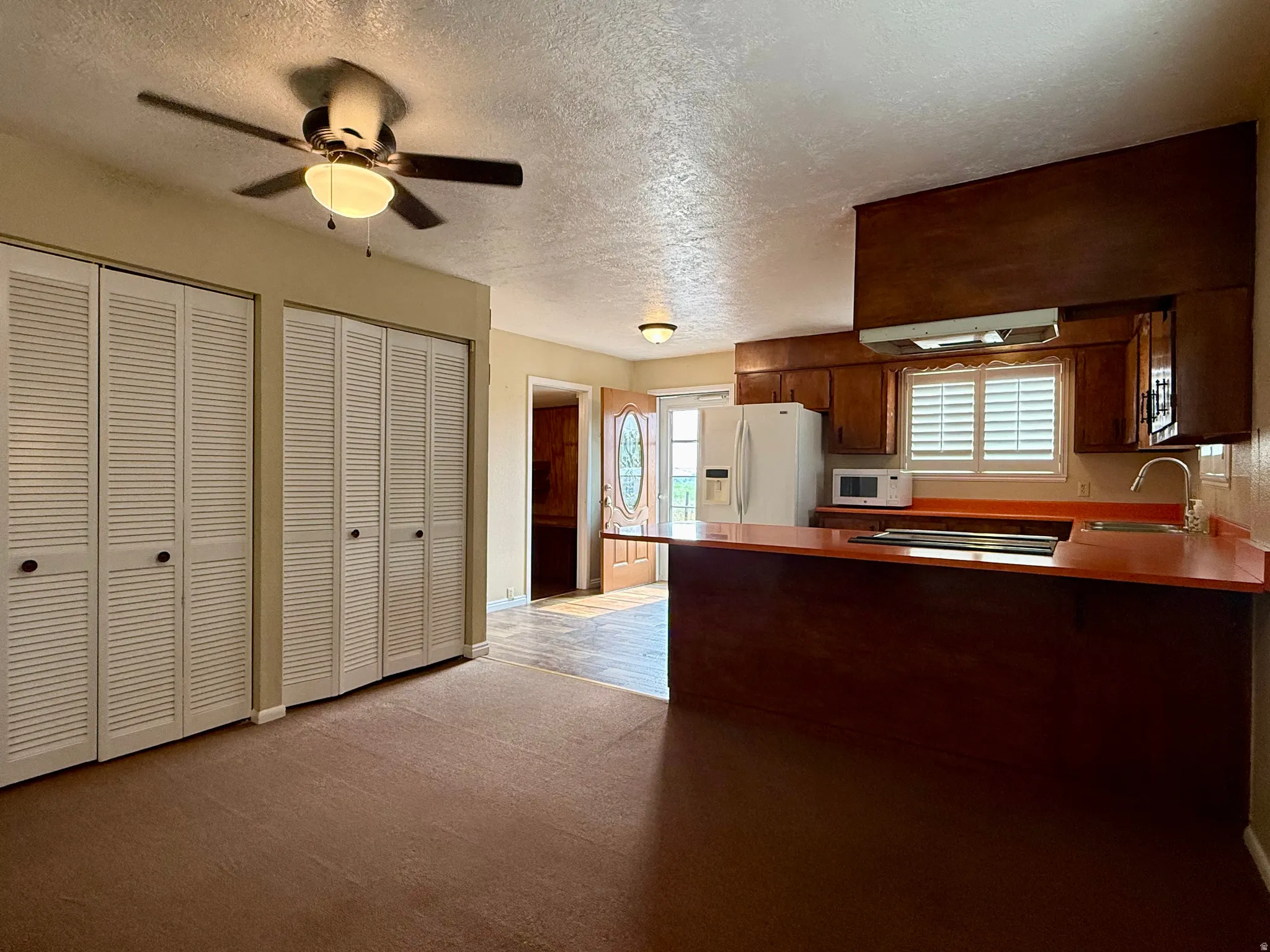 Open-concept kitchen and living area featuring warm wood cabinetry, a breakfast bar with solid surface countertops, and white louvered bifold doors