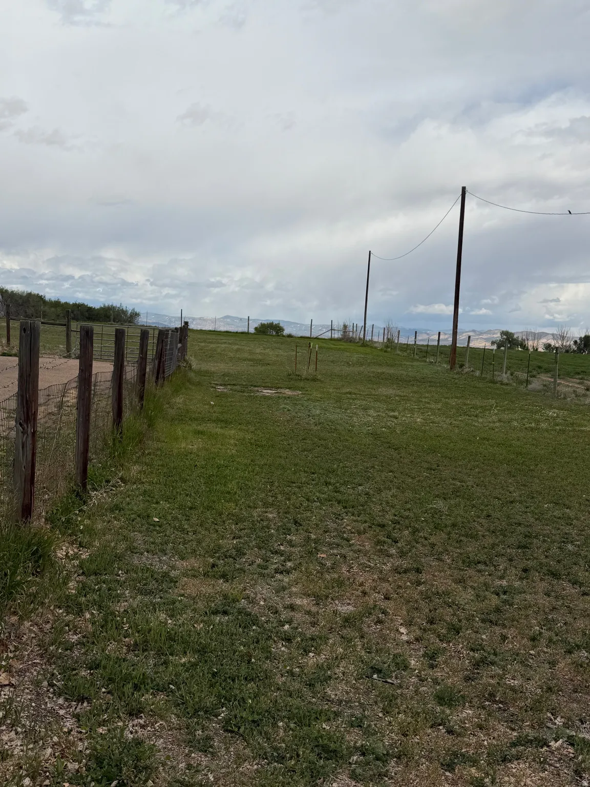 Expansive green space featuring a rustic wooden fence line and distant mountain formations