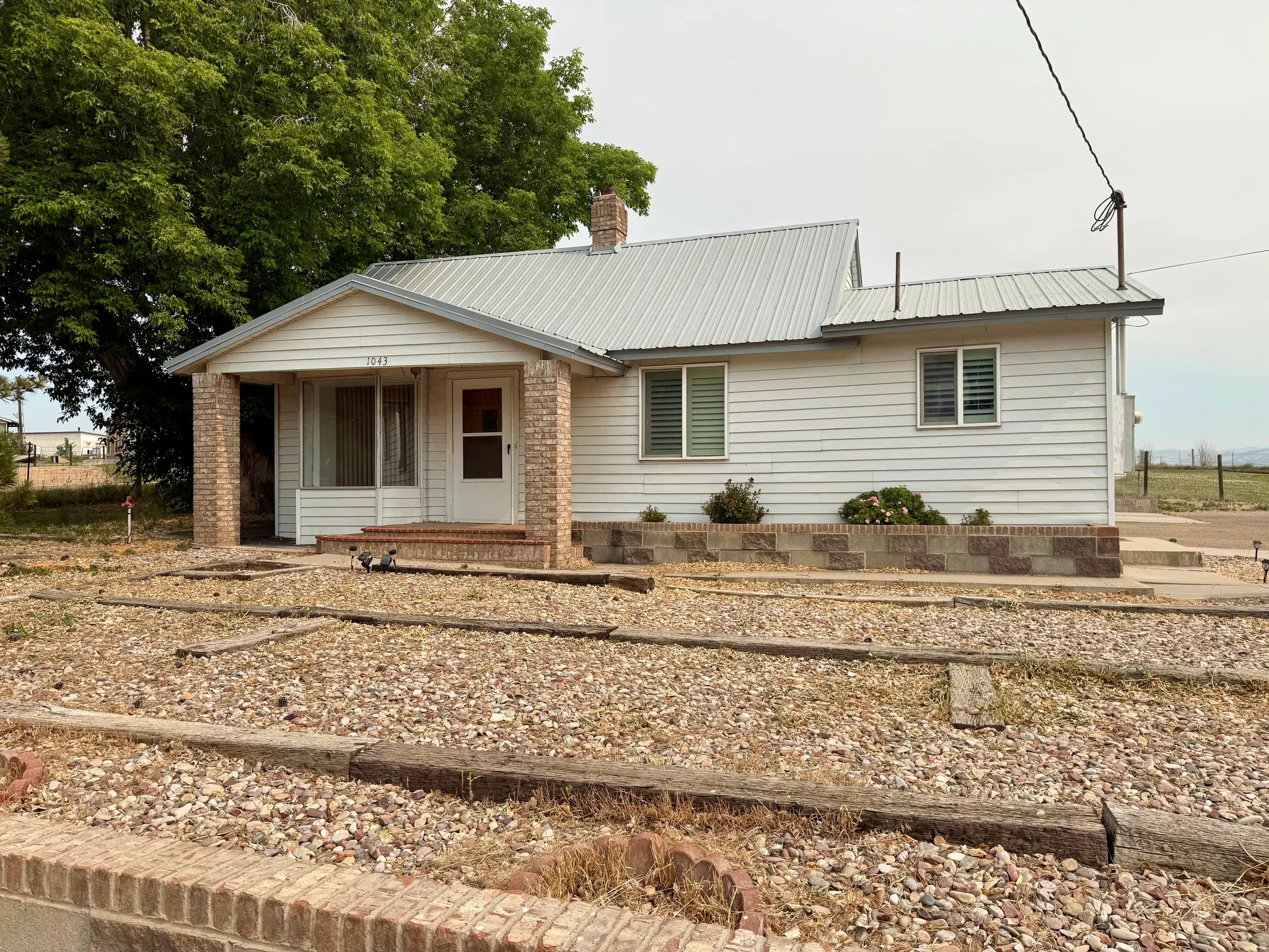 White siding exterior with a metal roof and a covered brick-columned porch