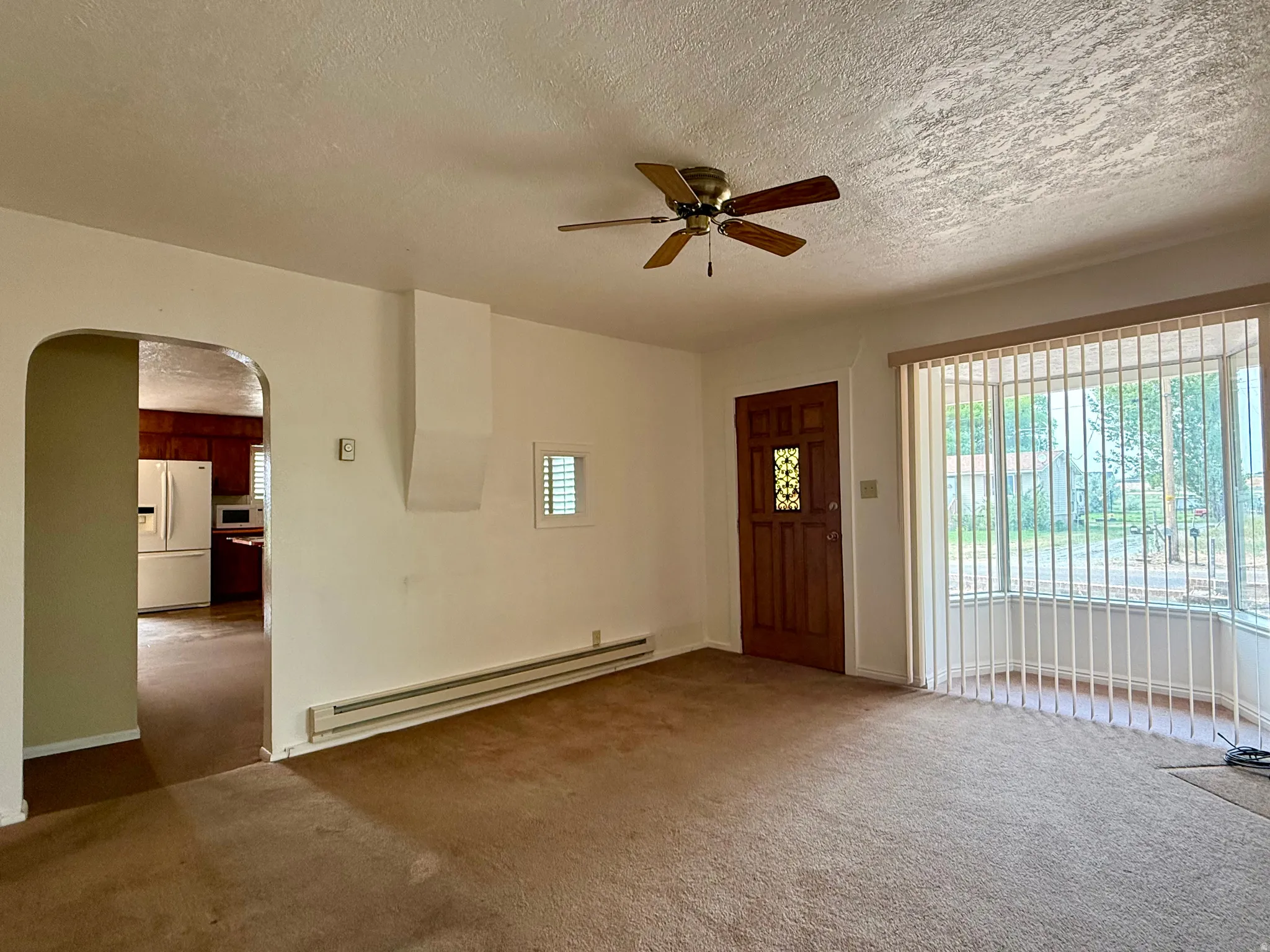 Living area featuring a bay window, ceiling fan, and an arched doorway leading to a kitchen with wood cabinetry