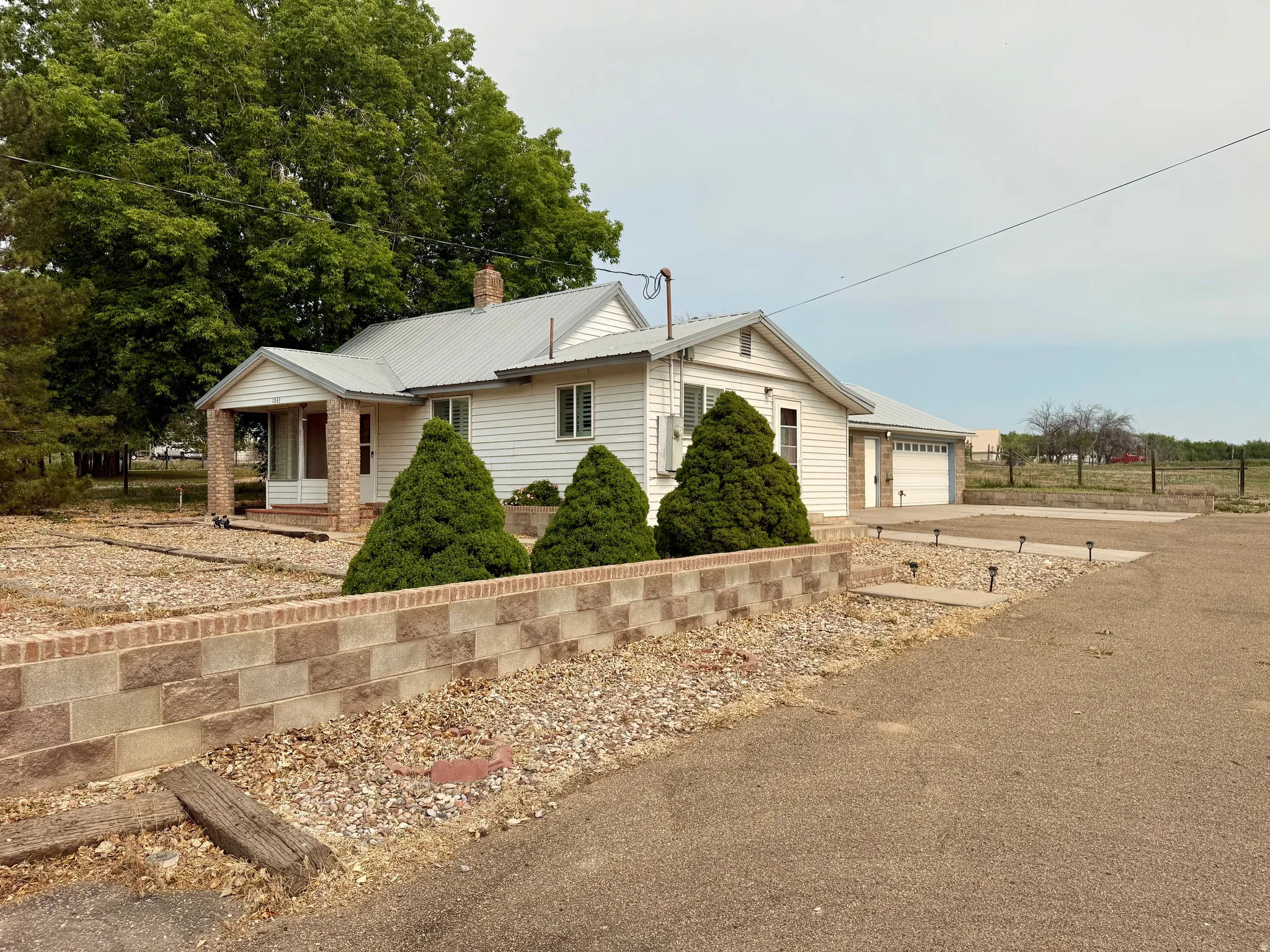 White siding residence featuring a metal roof, an attached two-car garage, and a brick-columned front porch